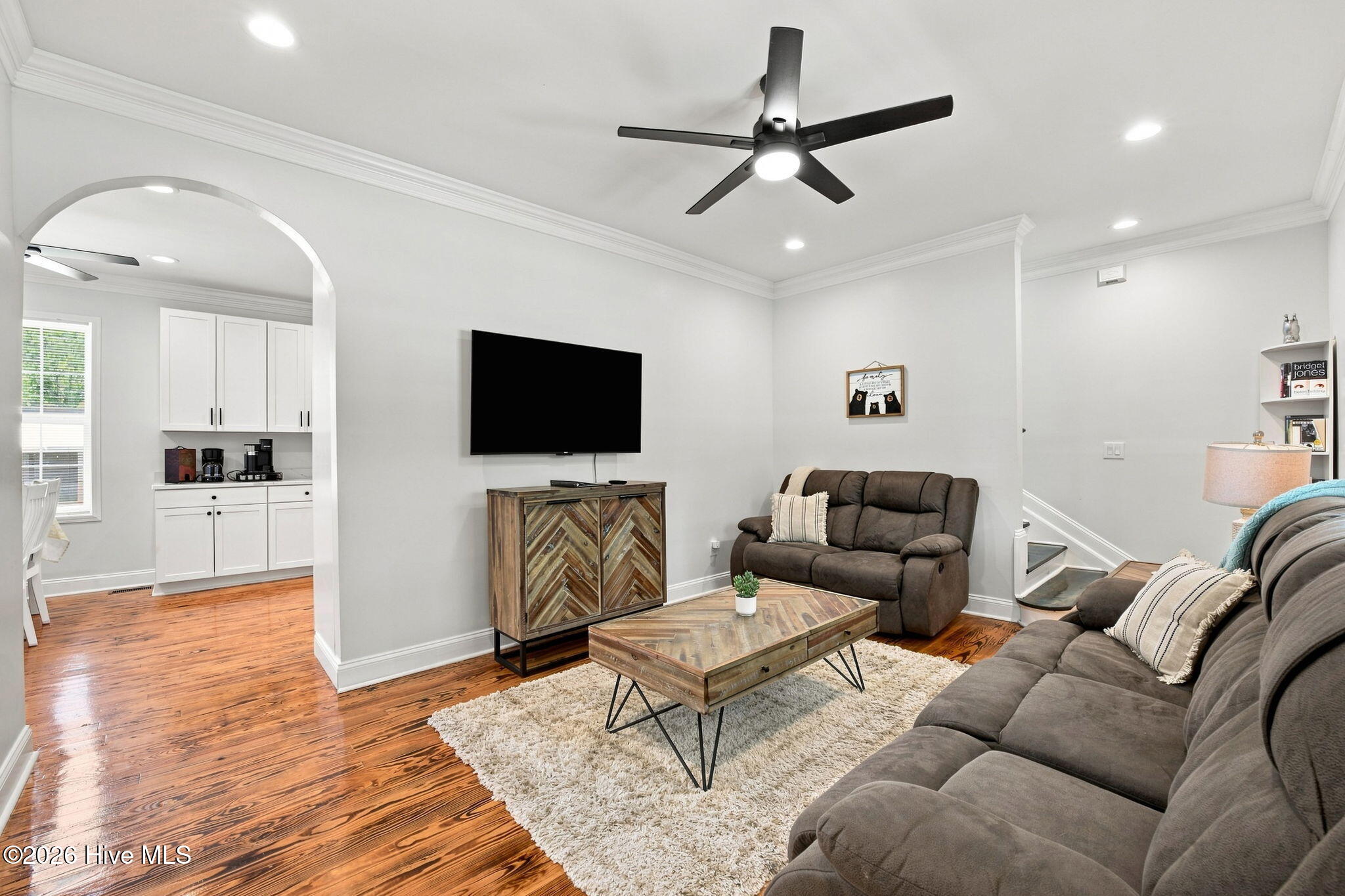 Furnished living room with gray sofas, a wall-mounted TV, and an arched opening to a coffee station.