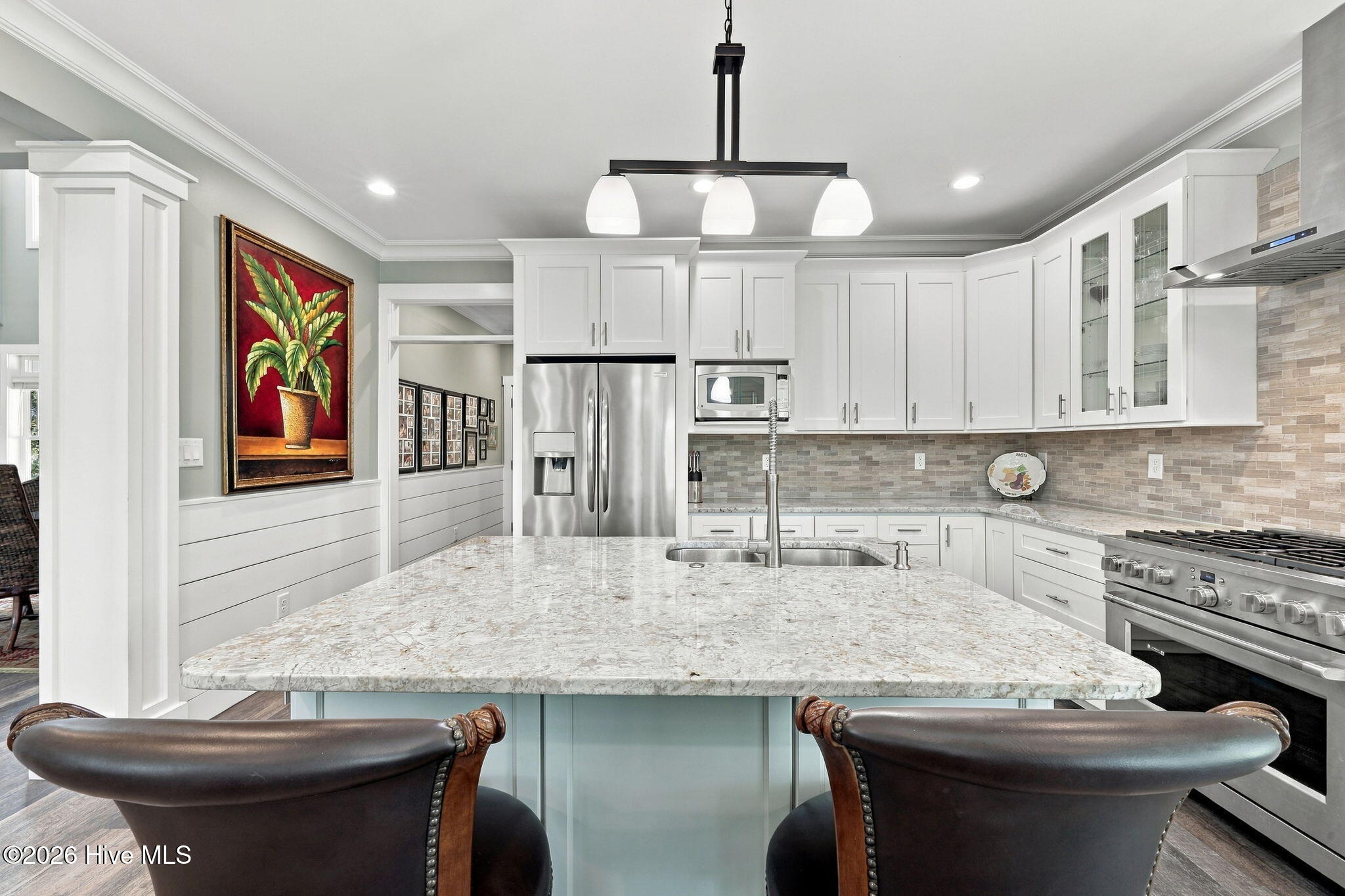 Kitchen with white cabinetry, a large stone island, stainless steel appliances, and dark leather bar chairs.