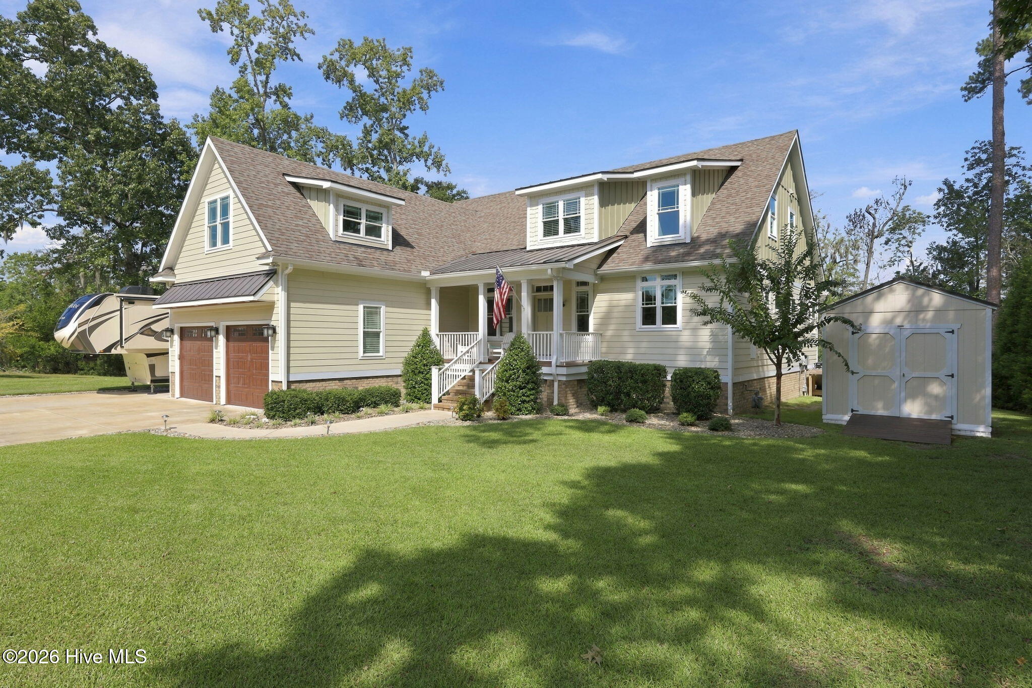 Pale yellow two-story home with a covered porch, travel trailer, and detached storage shed.