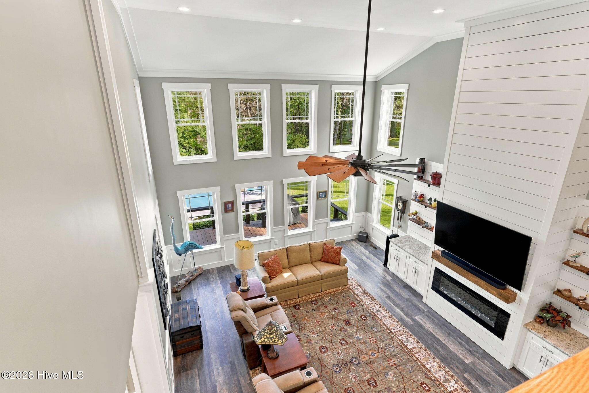 Two-story living room with tall windows, a ceiling fan, and a white fireplace and entertainment wall.