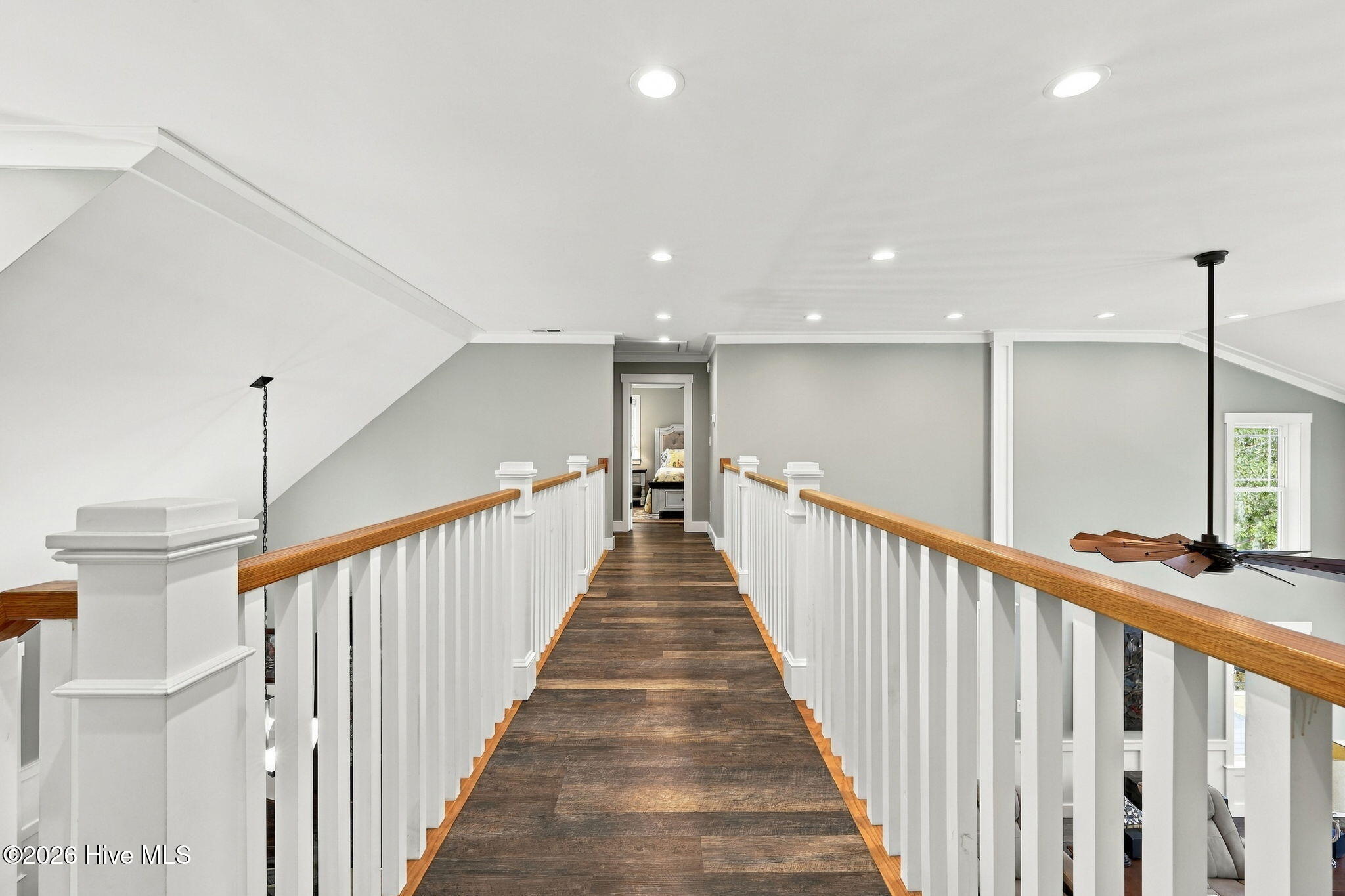 Upstairs landing with a dark wood walkway, white railings, and a bedroom doorway at the far end.
