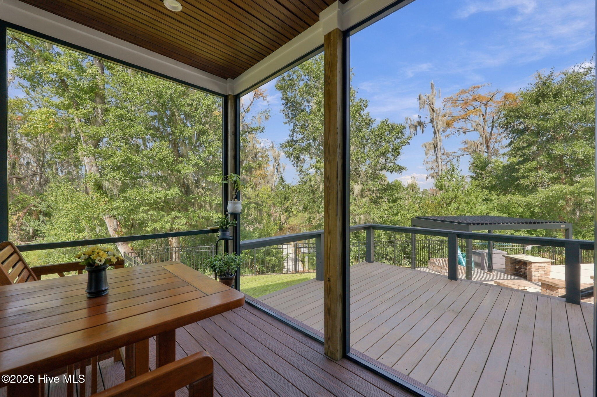 Glass-enclosed porch opening onto a deck with a stone fire feature and wooded views.