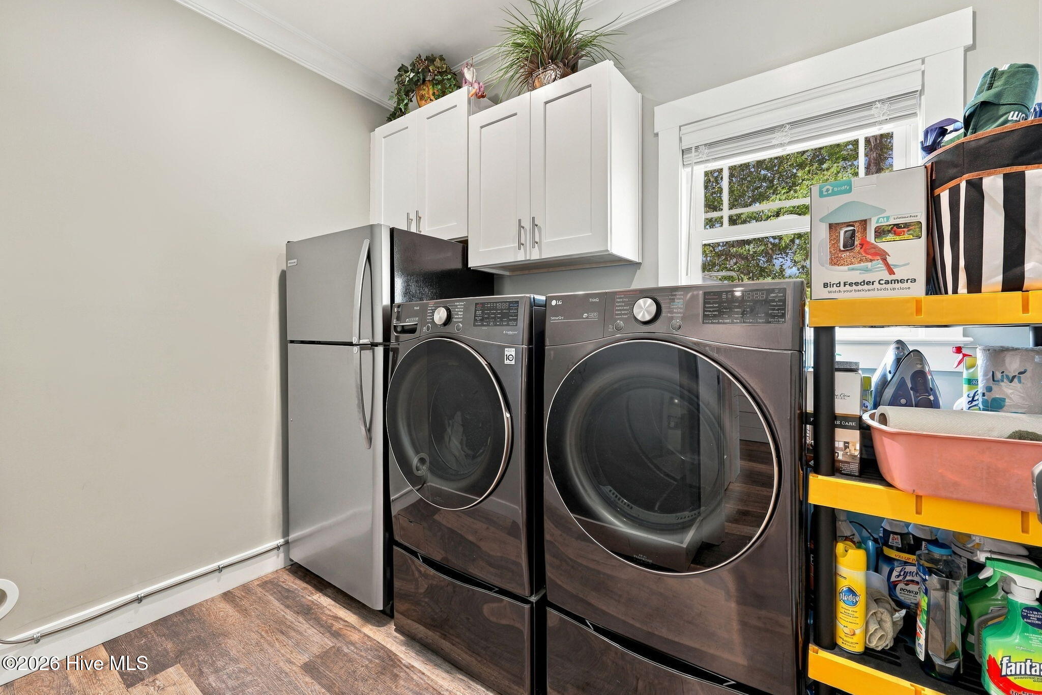 Laundry room with front-loading washer and dryer, refrigerator, white cabinets, and utility shelving.
