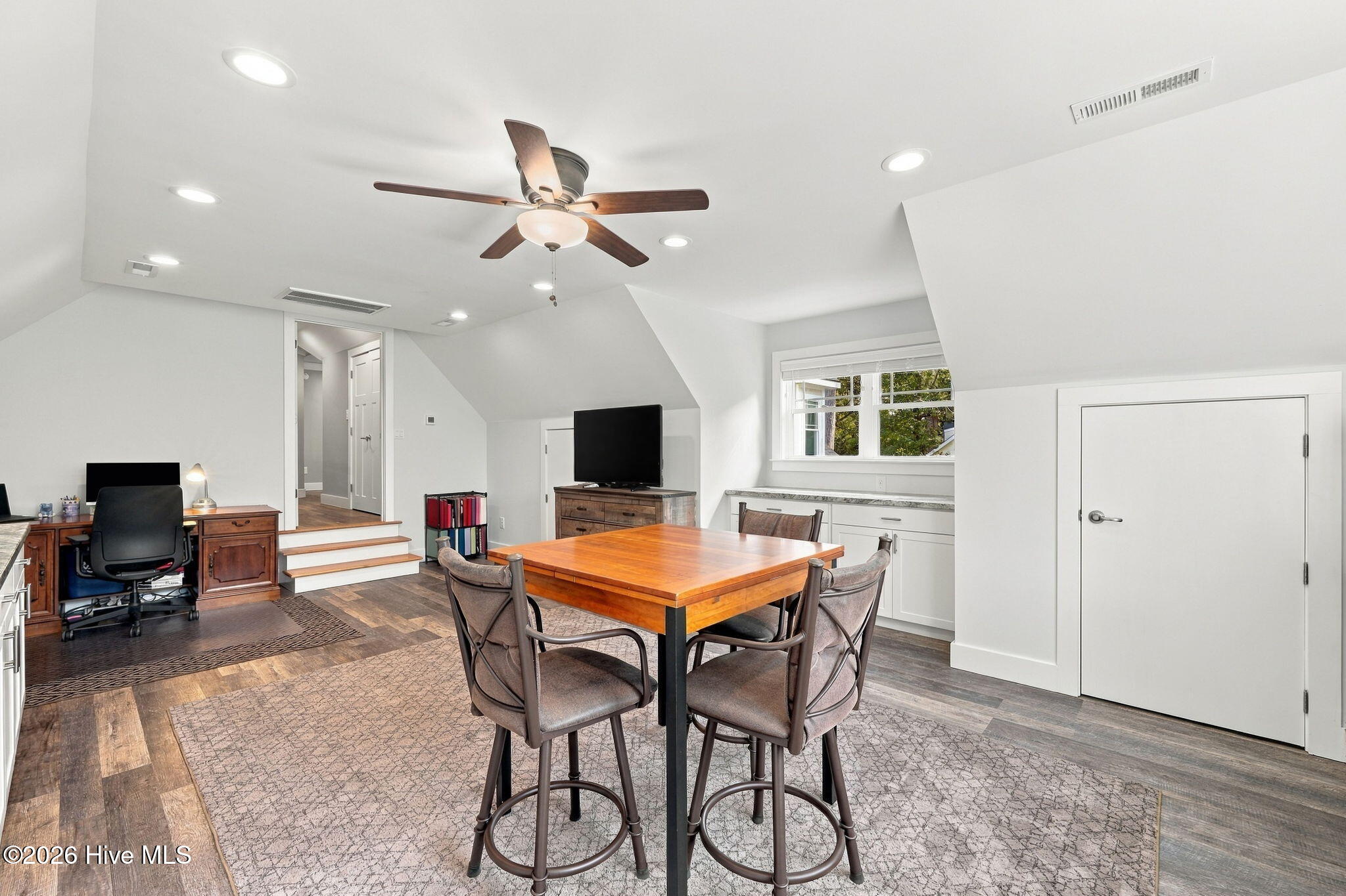 Furnished bonus room with a central table, office desk, TV, and built-in cabinets.