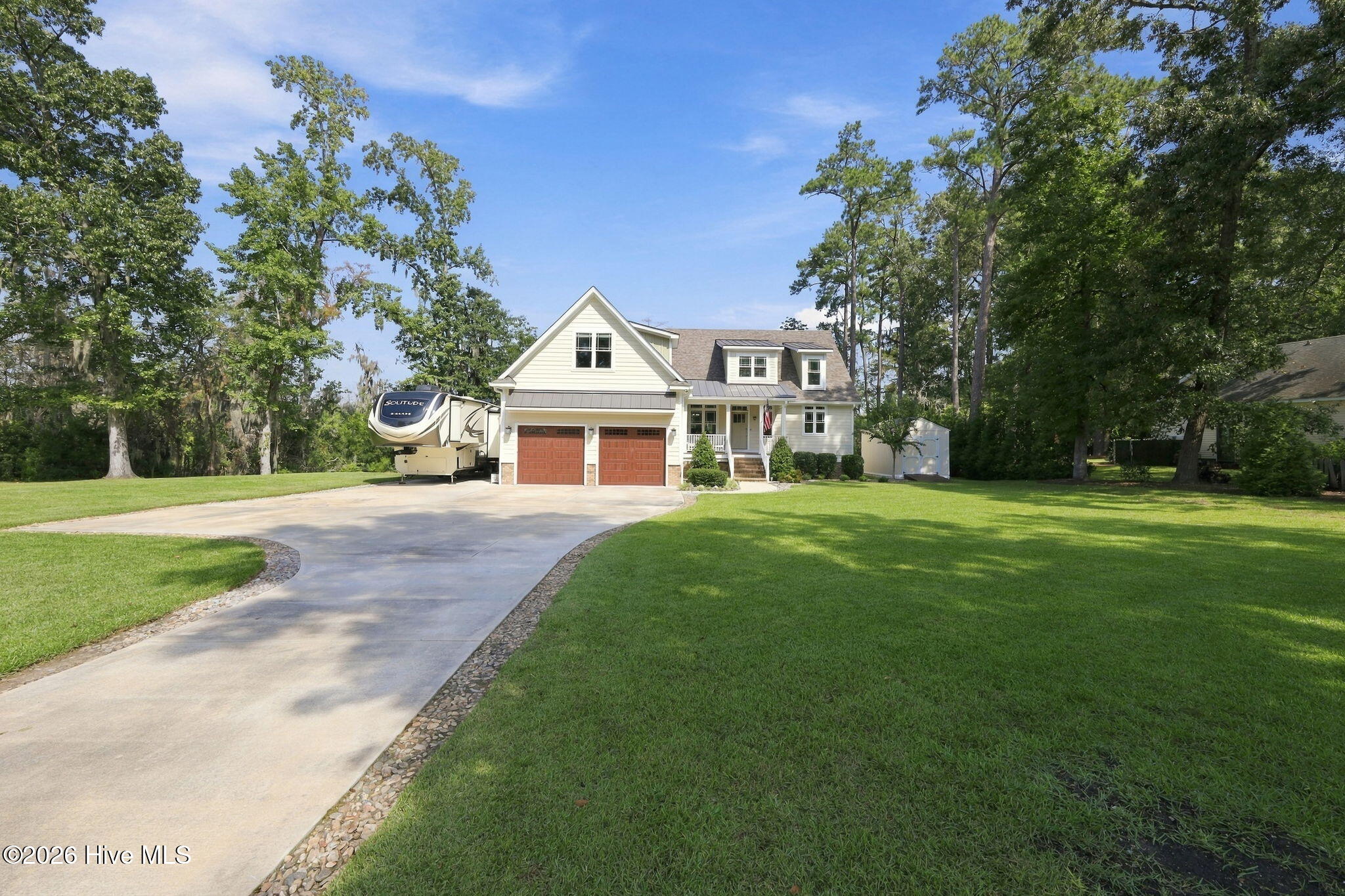 Two-story house with a broad curved driveway, double garage, large lawn, and recreational vehicle beside it.