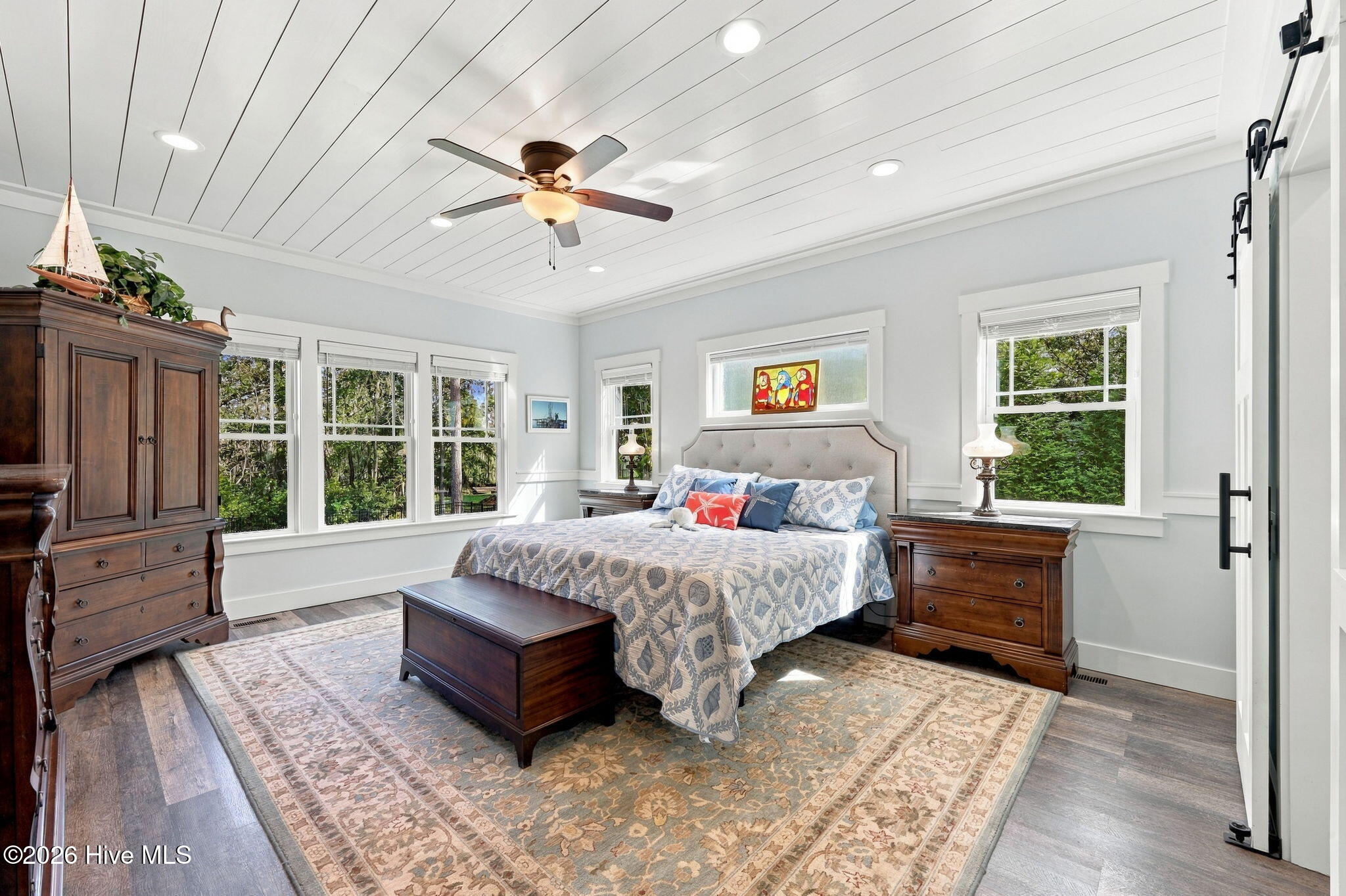 Furnished bedroom with a large patterned bed, dark wood furniture, and windows overlooking greenery.