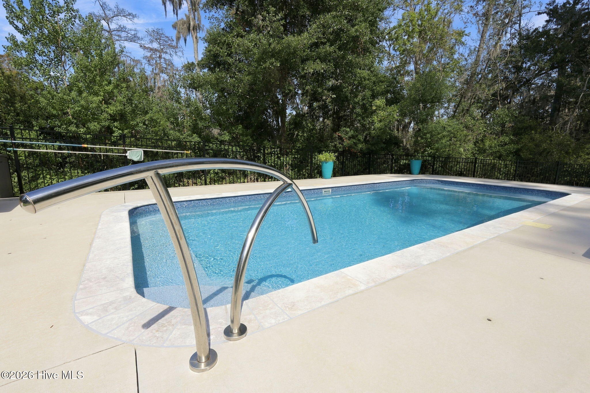 Backyard swimming pool with curved stainless steel handrails and a pale stone deck.