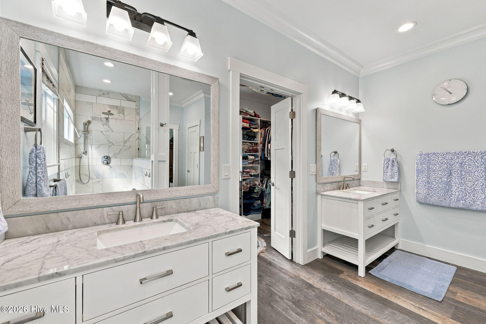 Bathroom with double vanities, marble-look counters, a large mirror, and a tiled glass shower.