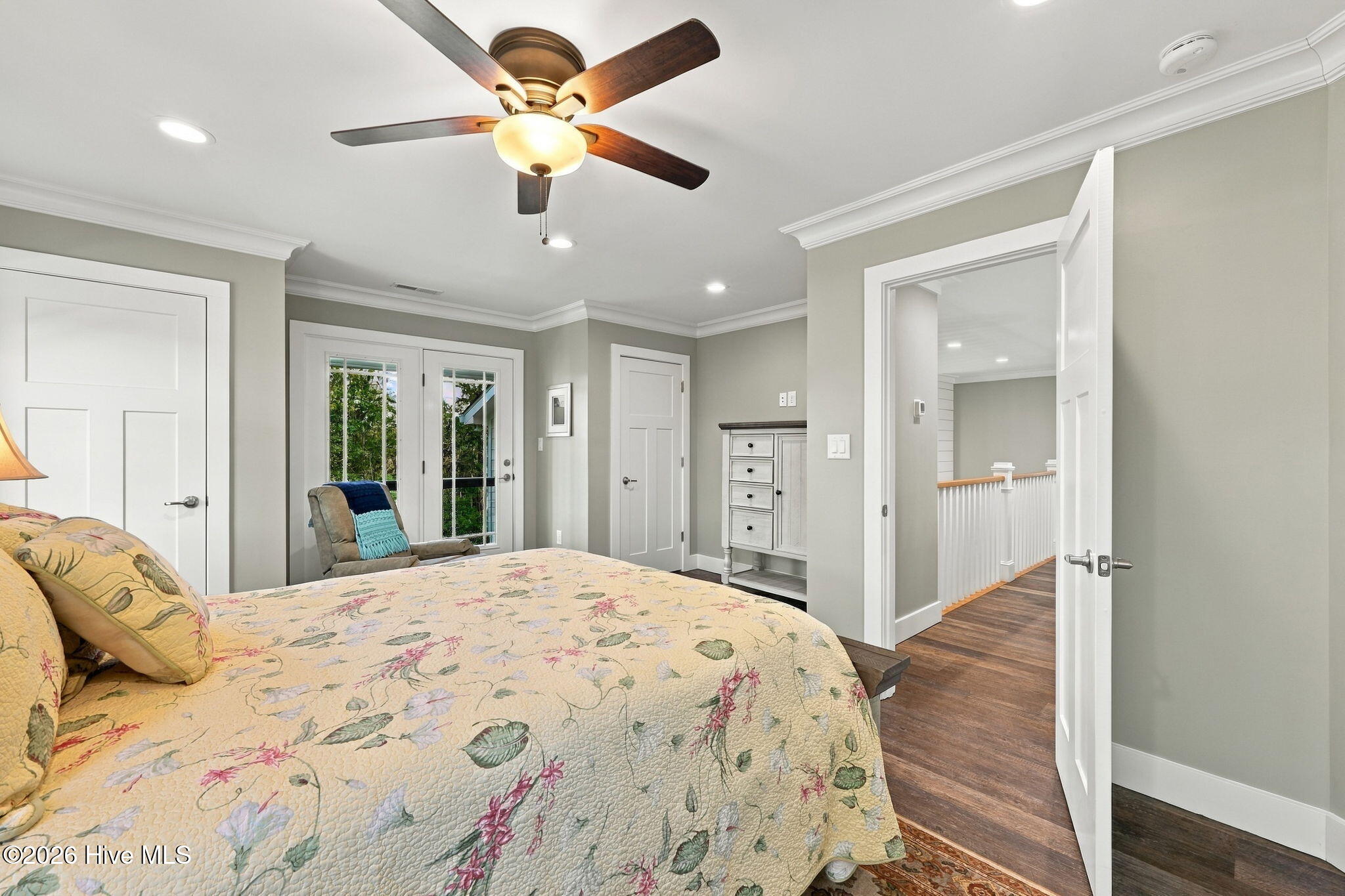 Furnished bedroom with a floral quilt-covered bed, ceiling fan, and French doors overlooking greenery.