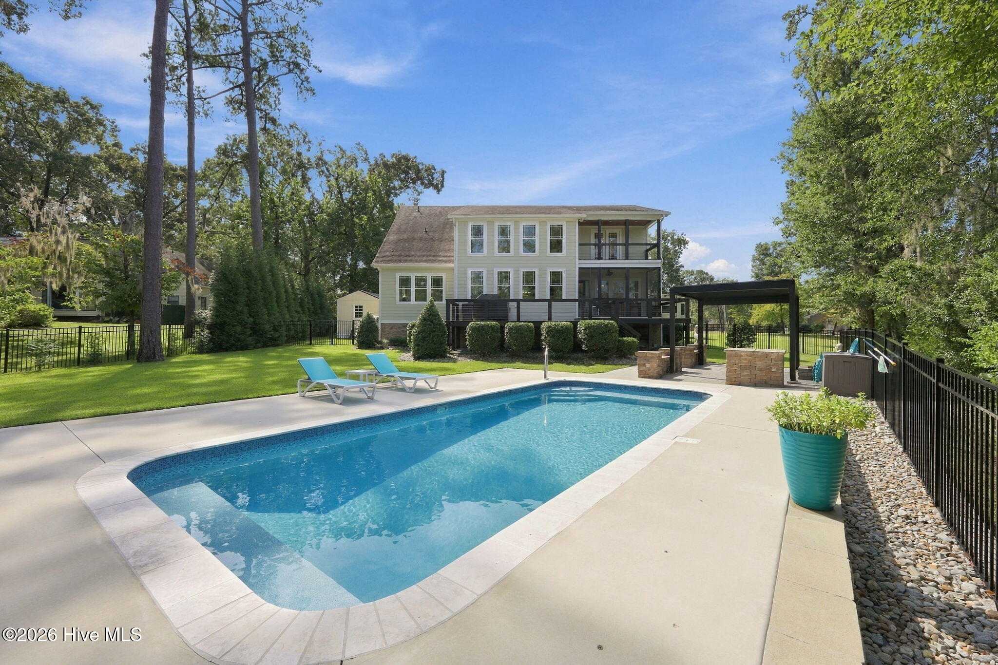Backyard swimming pool beside a two-story home, with a raised deck and covered patio.