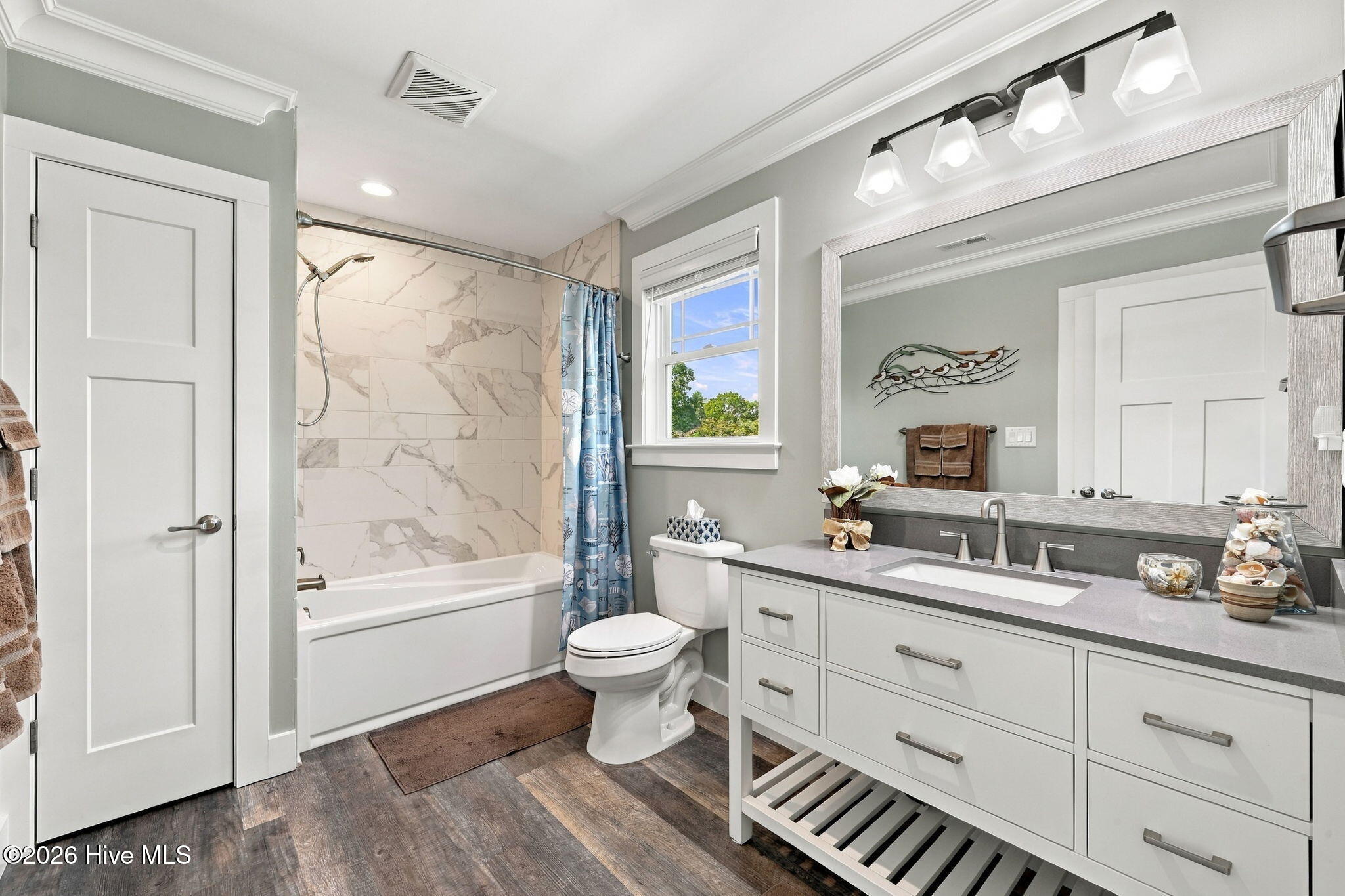 Bathroom with marble-look tub surround, blue shower curtain, and long vanity beneath a large mirror.