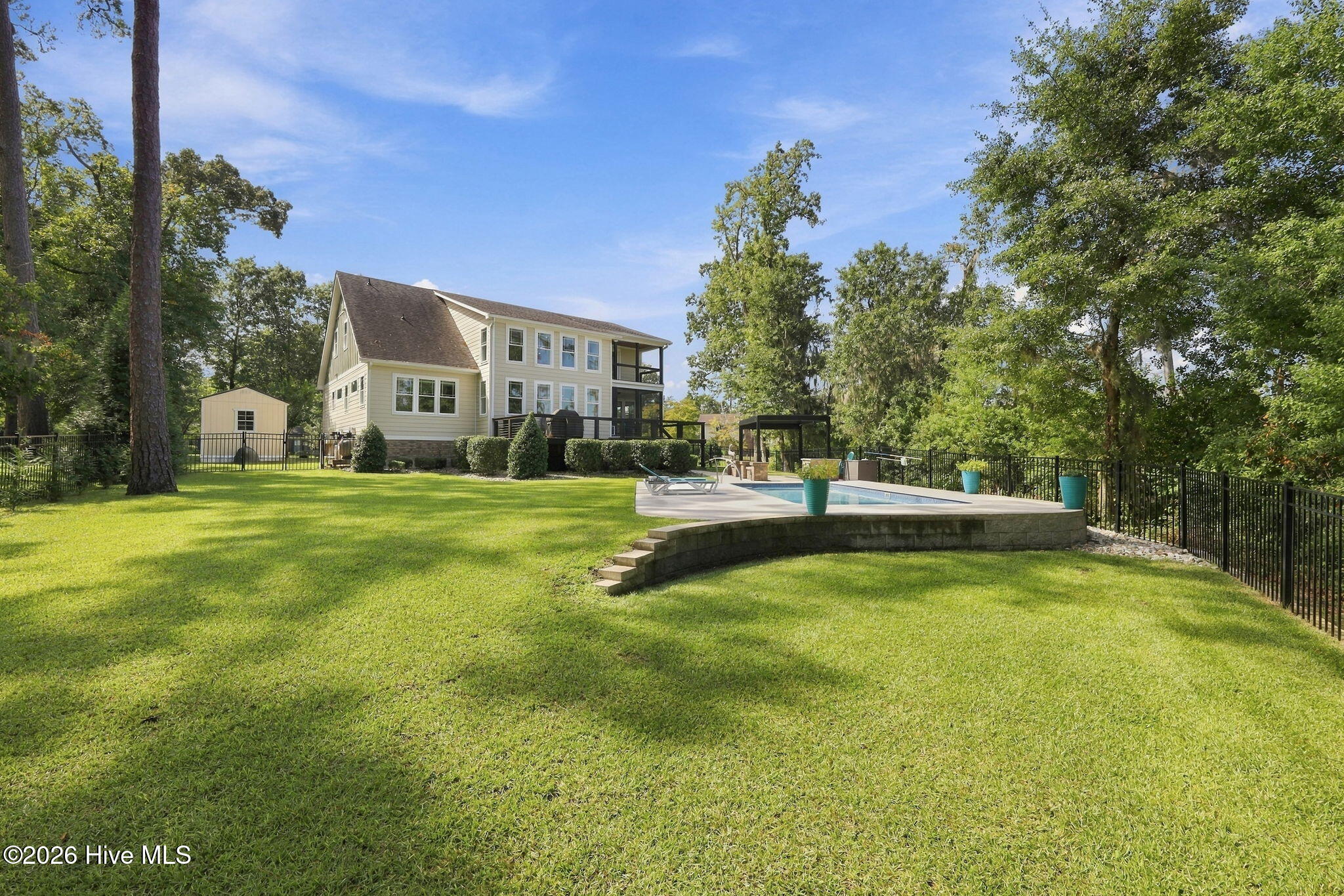 Two-story home overlooking a fenced pool and broad green lawn beneath mature trees.