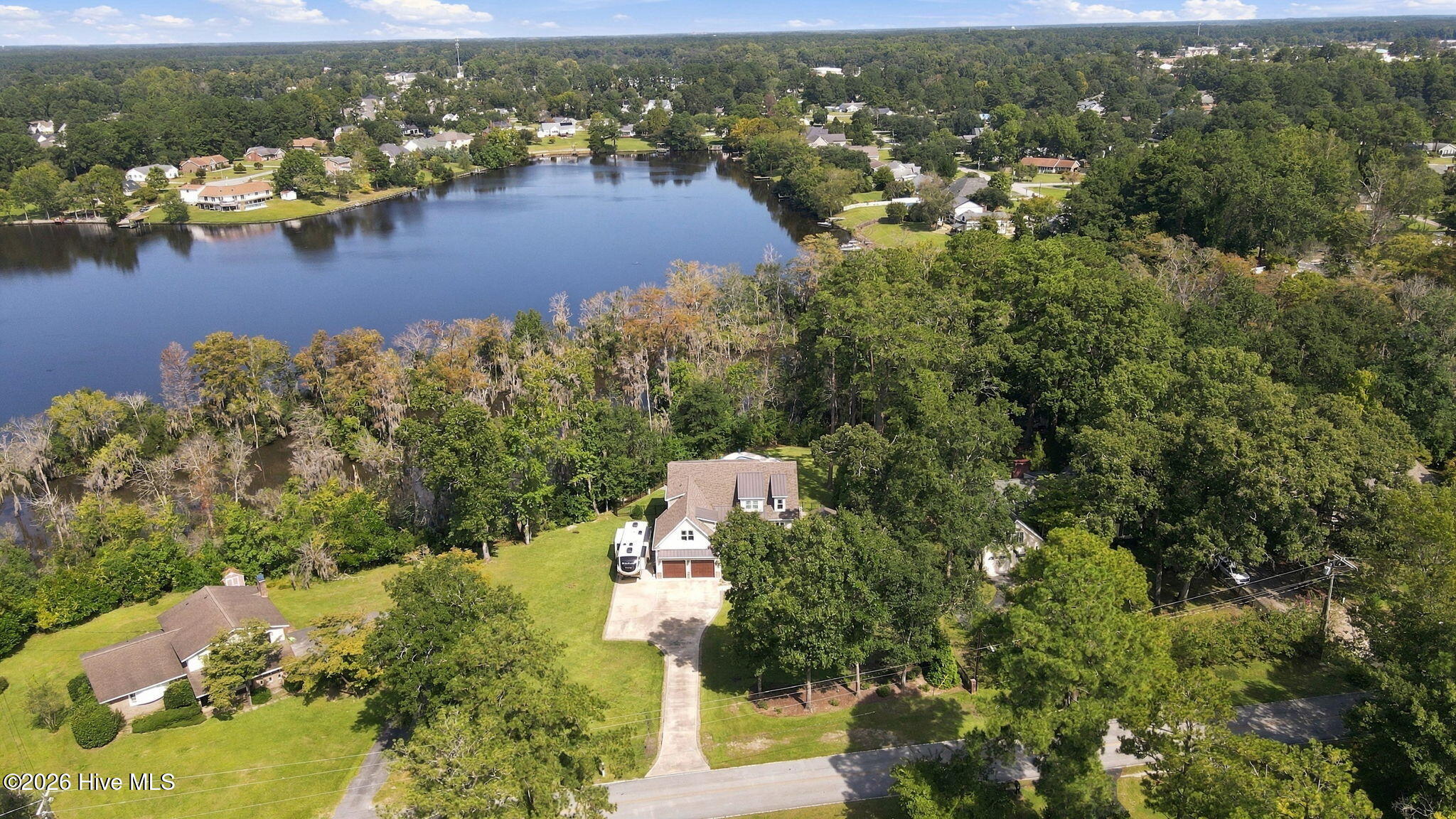Aerial view of a home beside a lake, with wooded shoreline and neighboring houses.