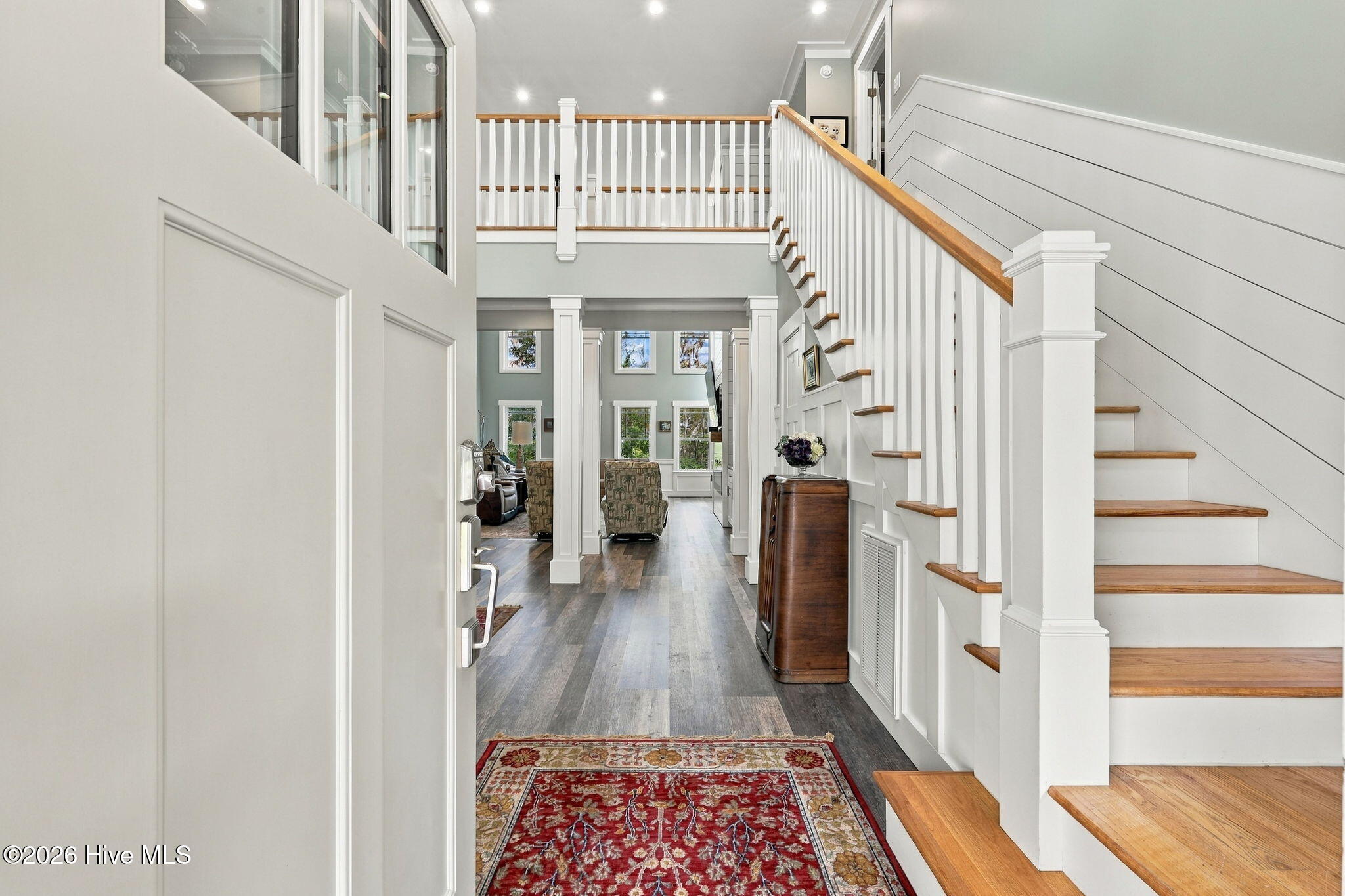 Two-story foyer with a white-railed staircase, wood treads, and a red patterned rug.