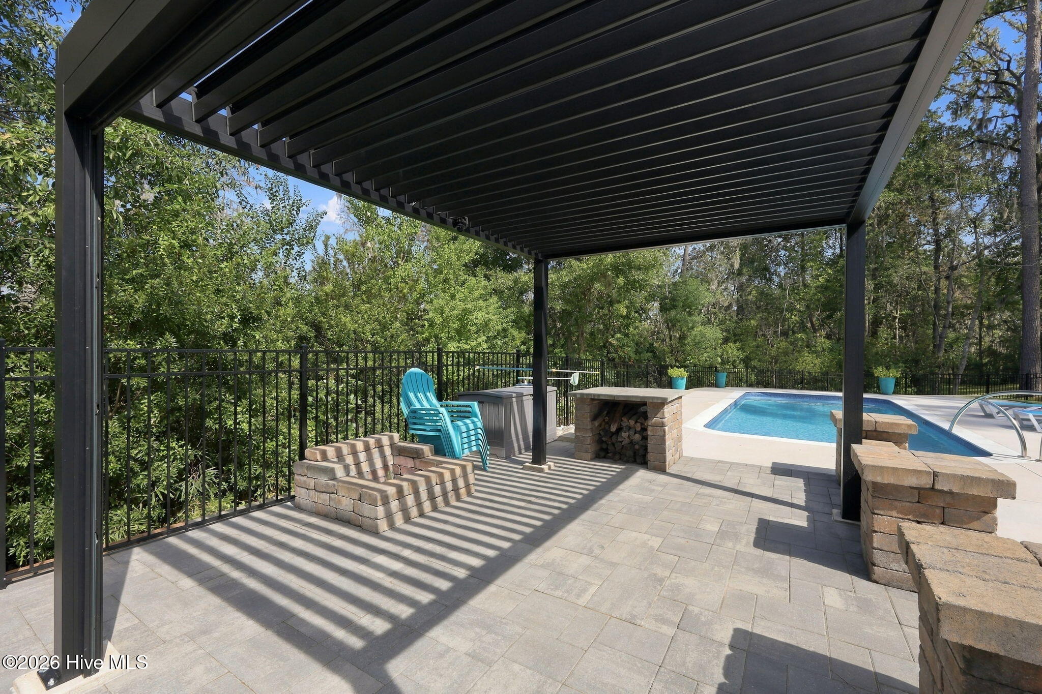 Pergola-covered patio beside a swimming pool, with stone seating walls and a built-in fireplace.
