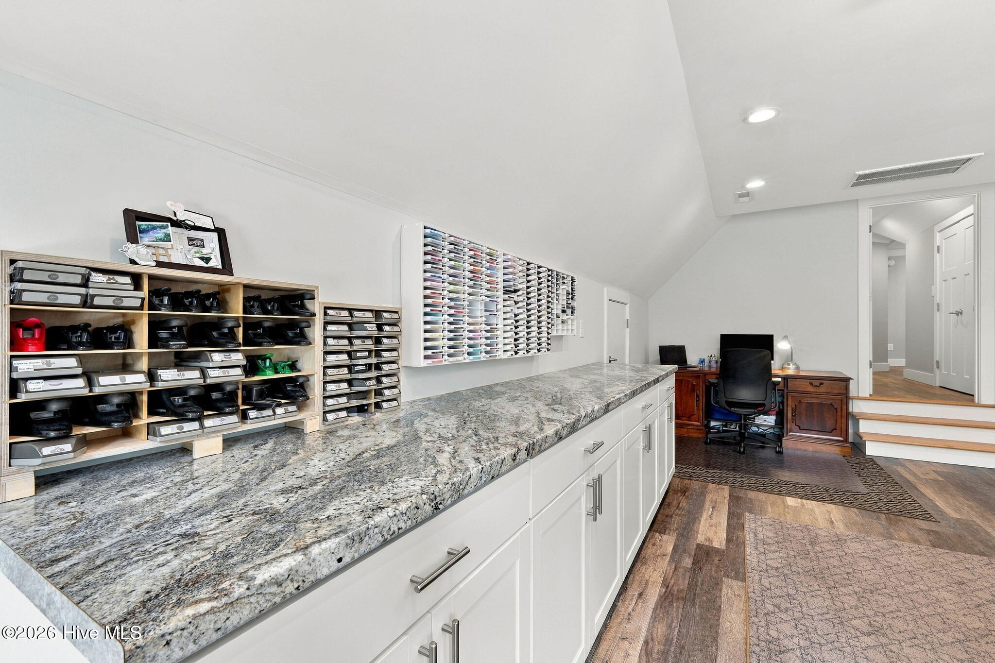 Workspace with a long granite counter, white cabinetry, wall organizers, and a desk.