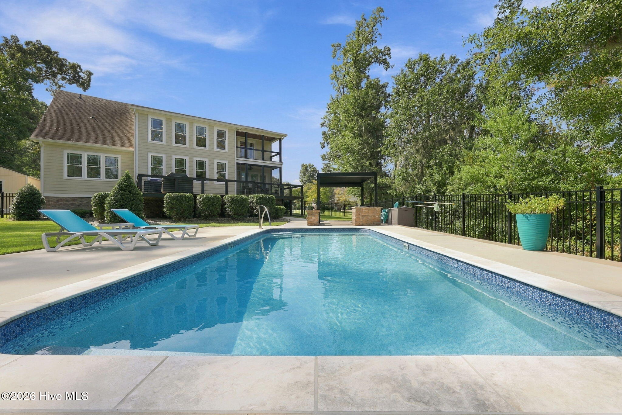 Backyard swimming pool with blue lounge chairs, stone patio, and a two-story house with decks.