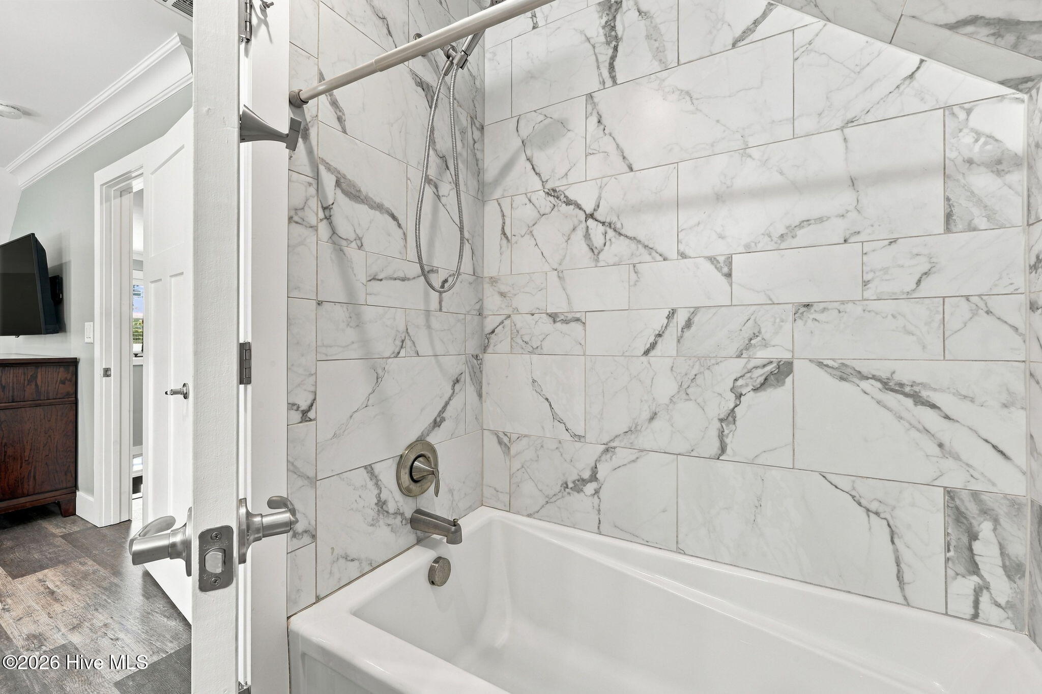 Bathroom tub with marble-look tile surround and handheld showerhead.
