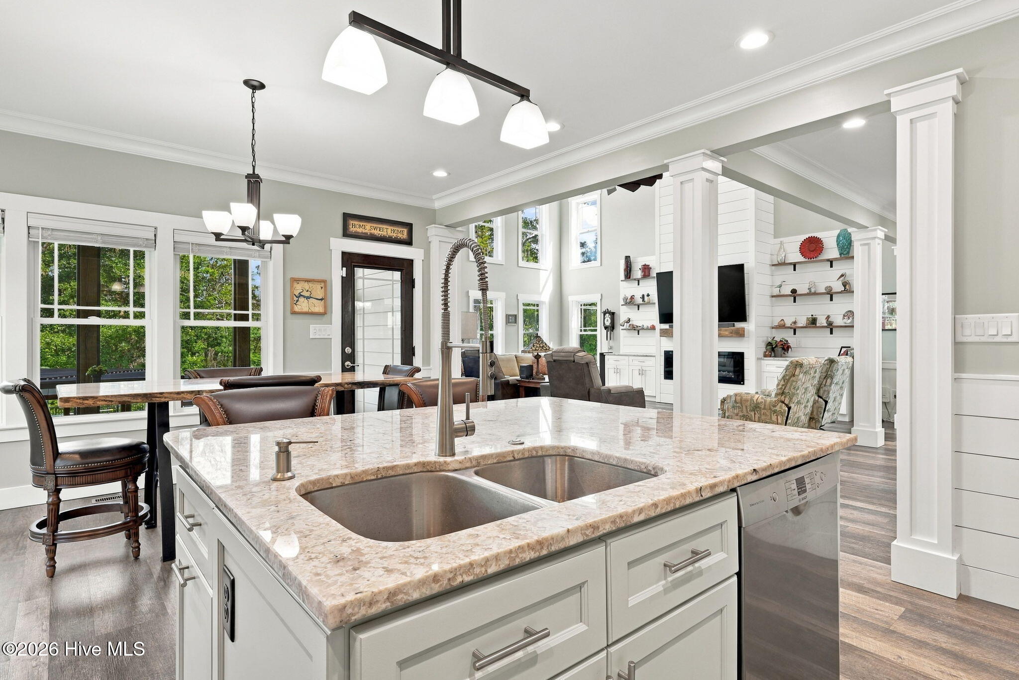 Open-plan kitchen with a large stone island and double sink overlooking a living room with built-in shelving.