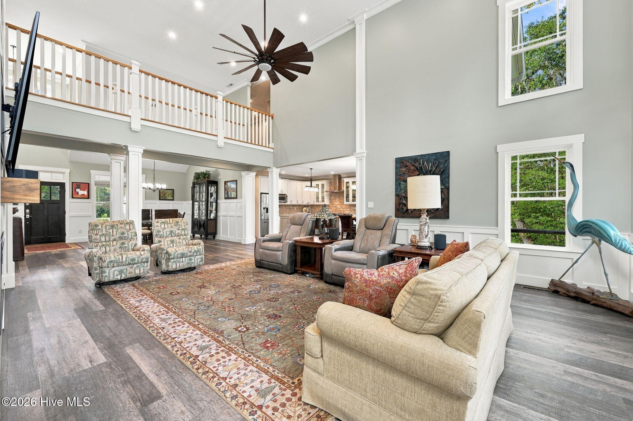 Two-story living room with a vaulted ceiling, upstairs balcony, patterned rug, and seating arranged around a coffee table.