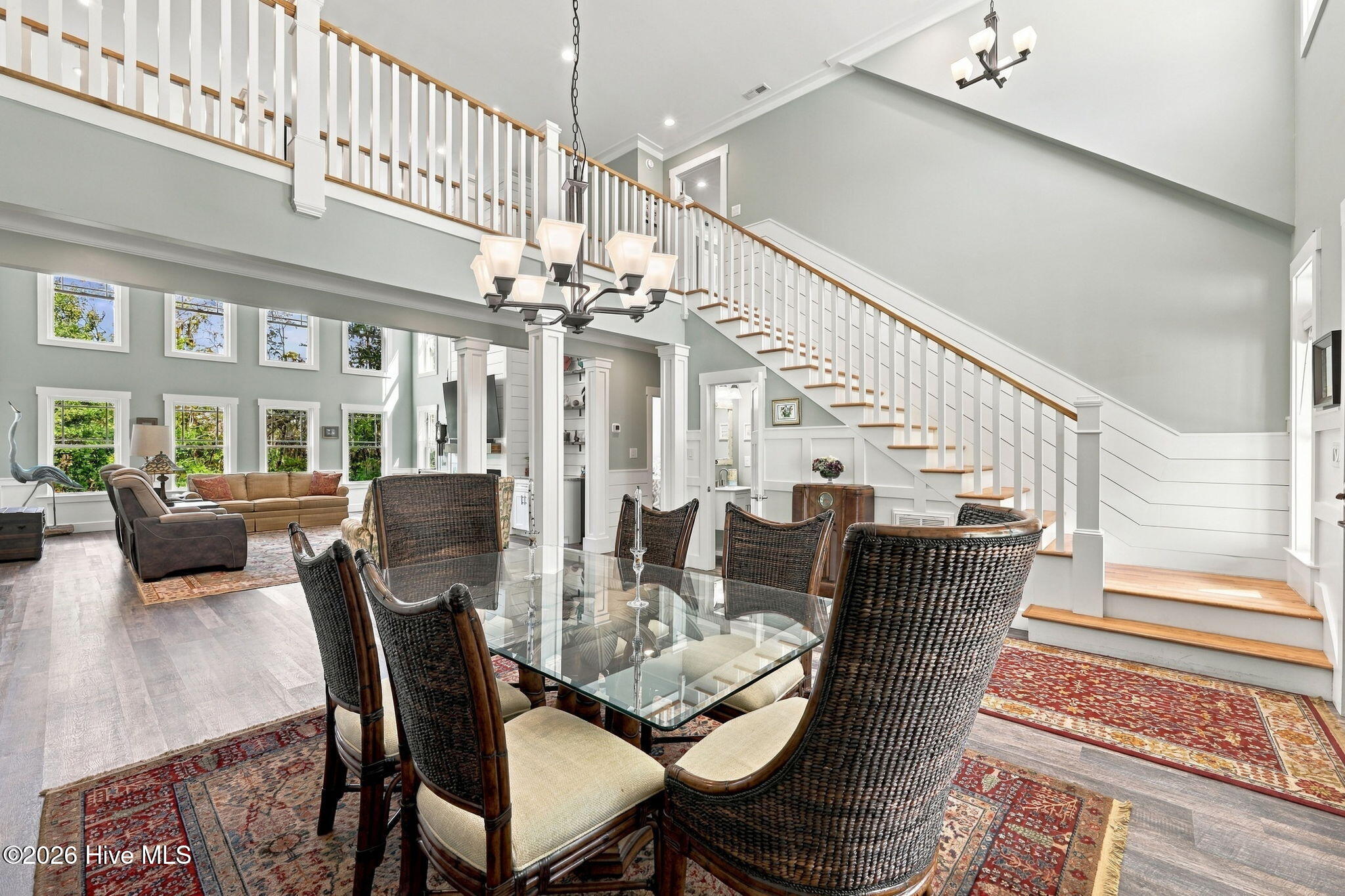 Open dining and living room with a glass-top table and sweeping staircase.