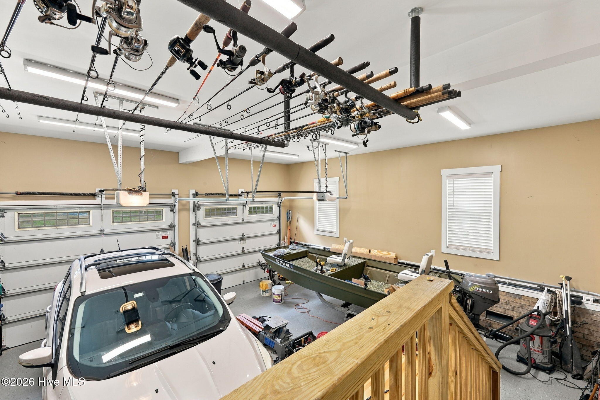Garage with a car, fishing boat, and rows of fishing rods suspended overhead.