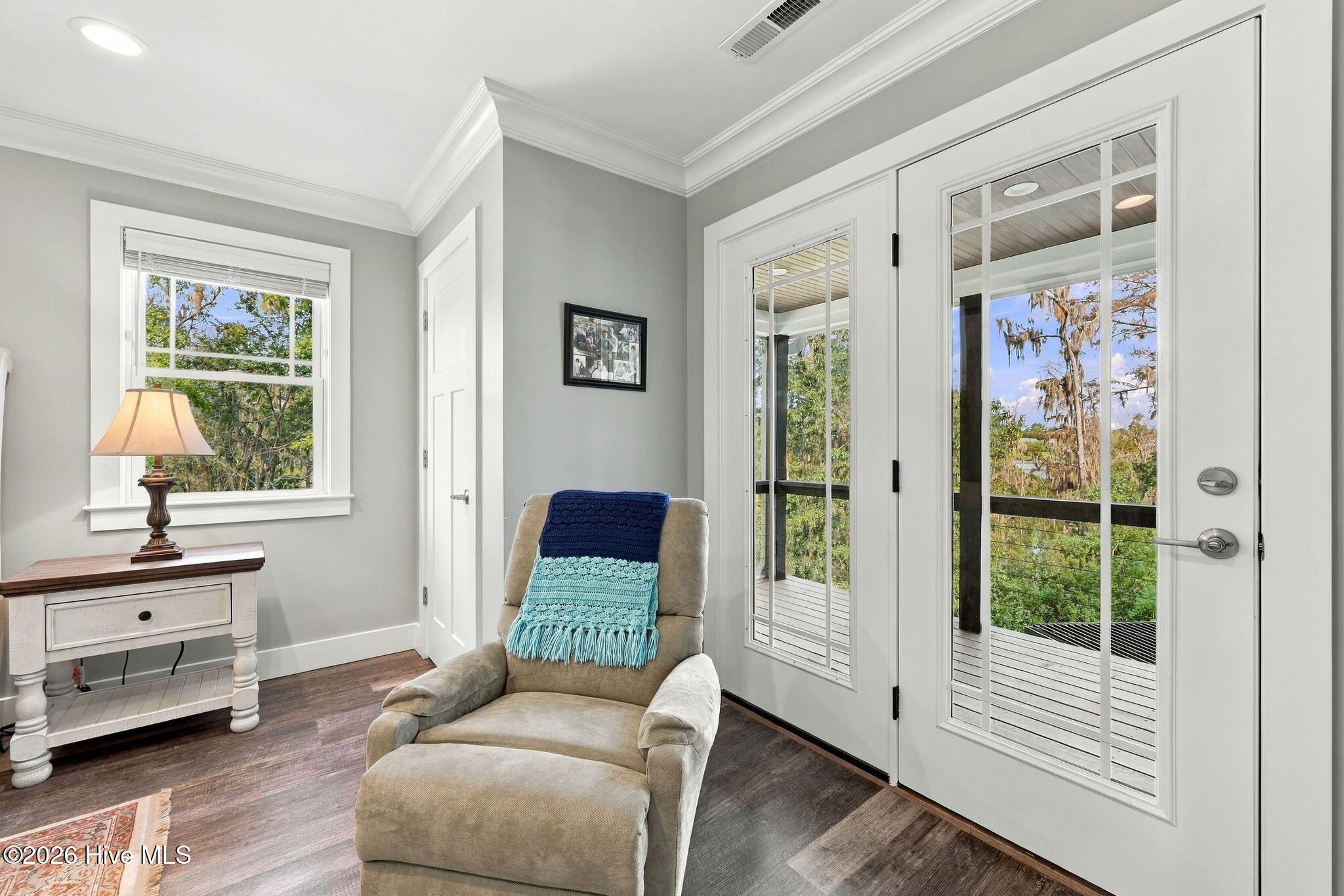 Furnished sitting room with a recliner beside glass doors opening to a tree-lined deck.
