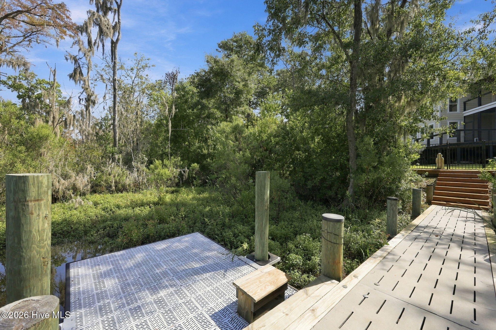 Dock and boardwalk beside a wooded marsh, with the house’s raised deck visible nearby.
