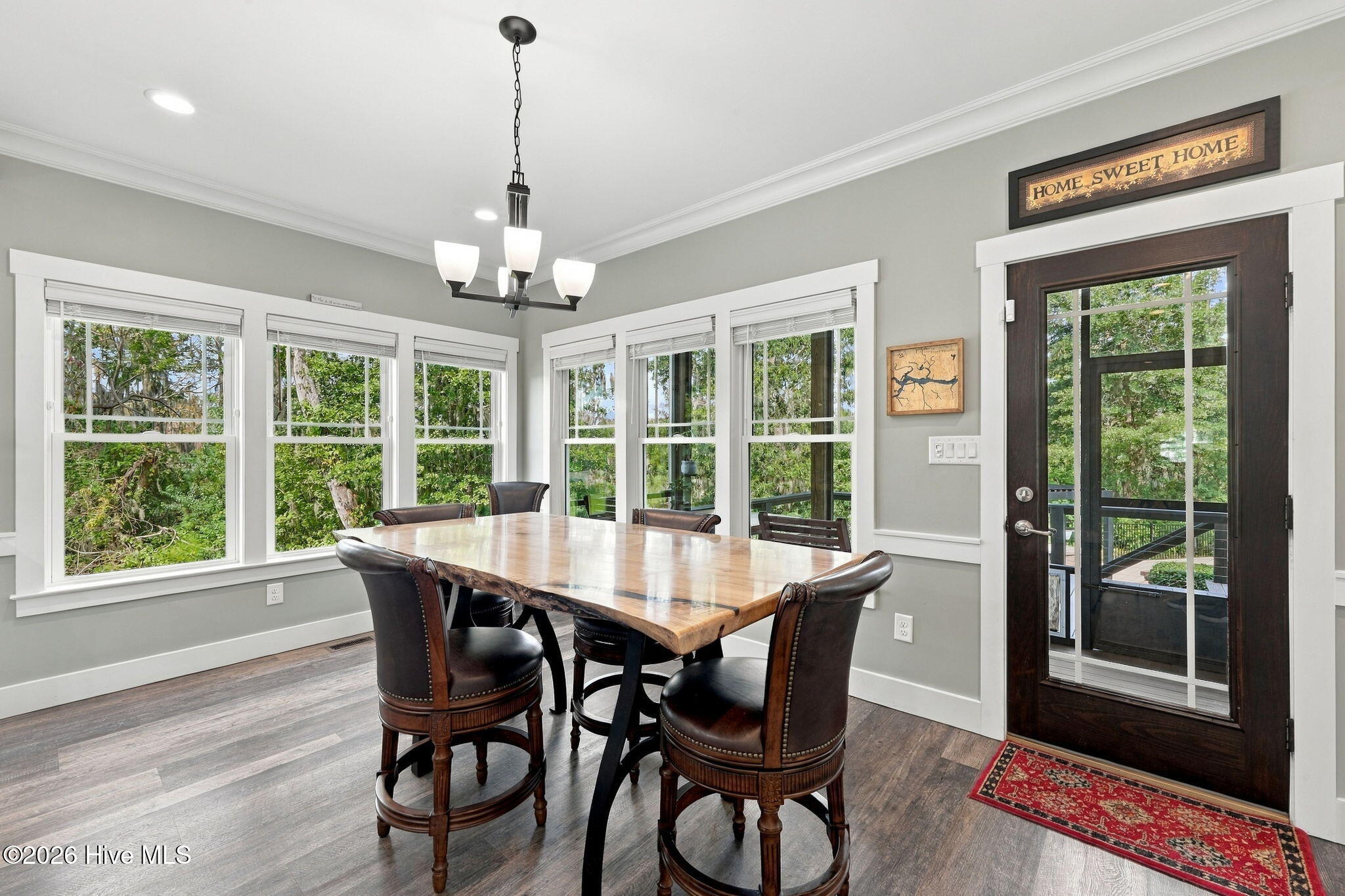 Dining room with a live-edge wood table, leather chairs, leafy views, and a glass-paneled deck door.