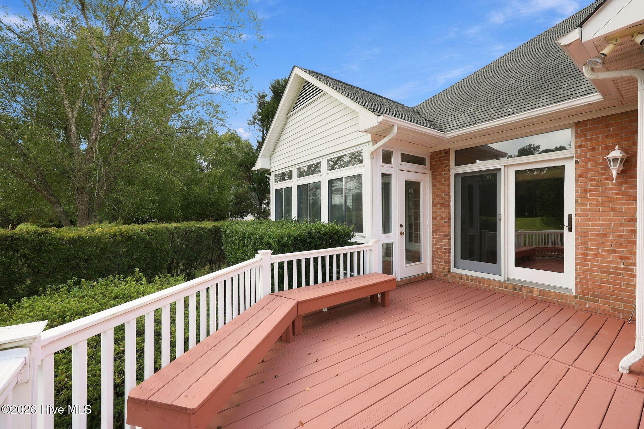 Reddish deck with a built-in bench and white railing beside a brick house.