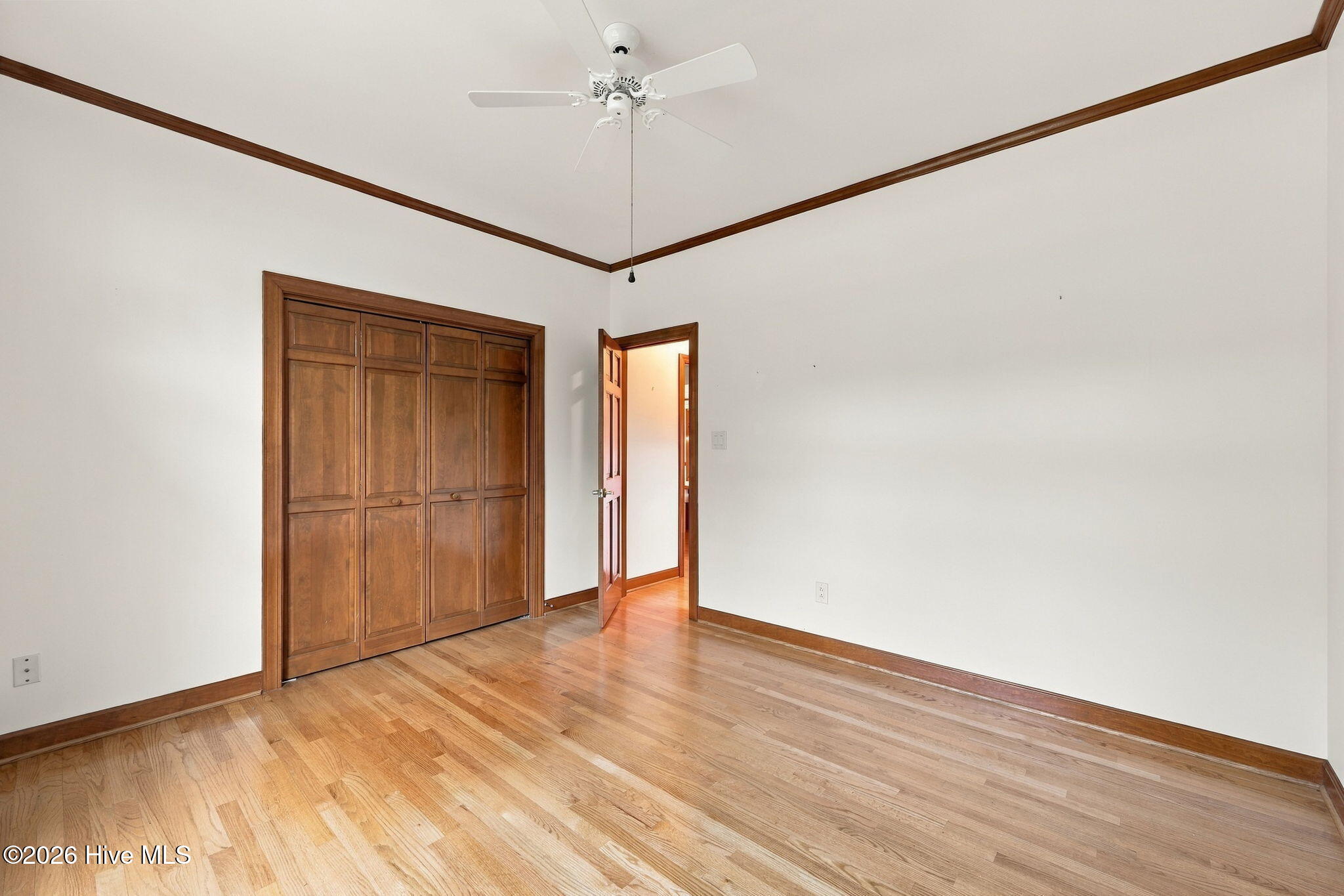 Empty bedroom with hardwood floors, a built-in wooden closet, and a ceiling fan.