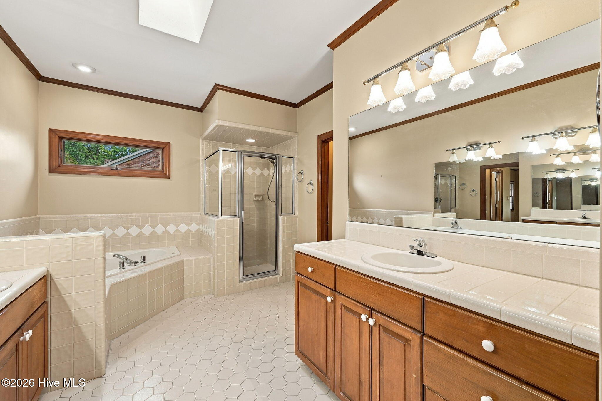 Spacious bathroom with tiled shower, built-in tub, and long wood vanity beneath a large mirror.