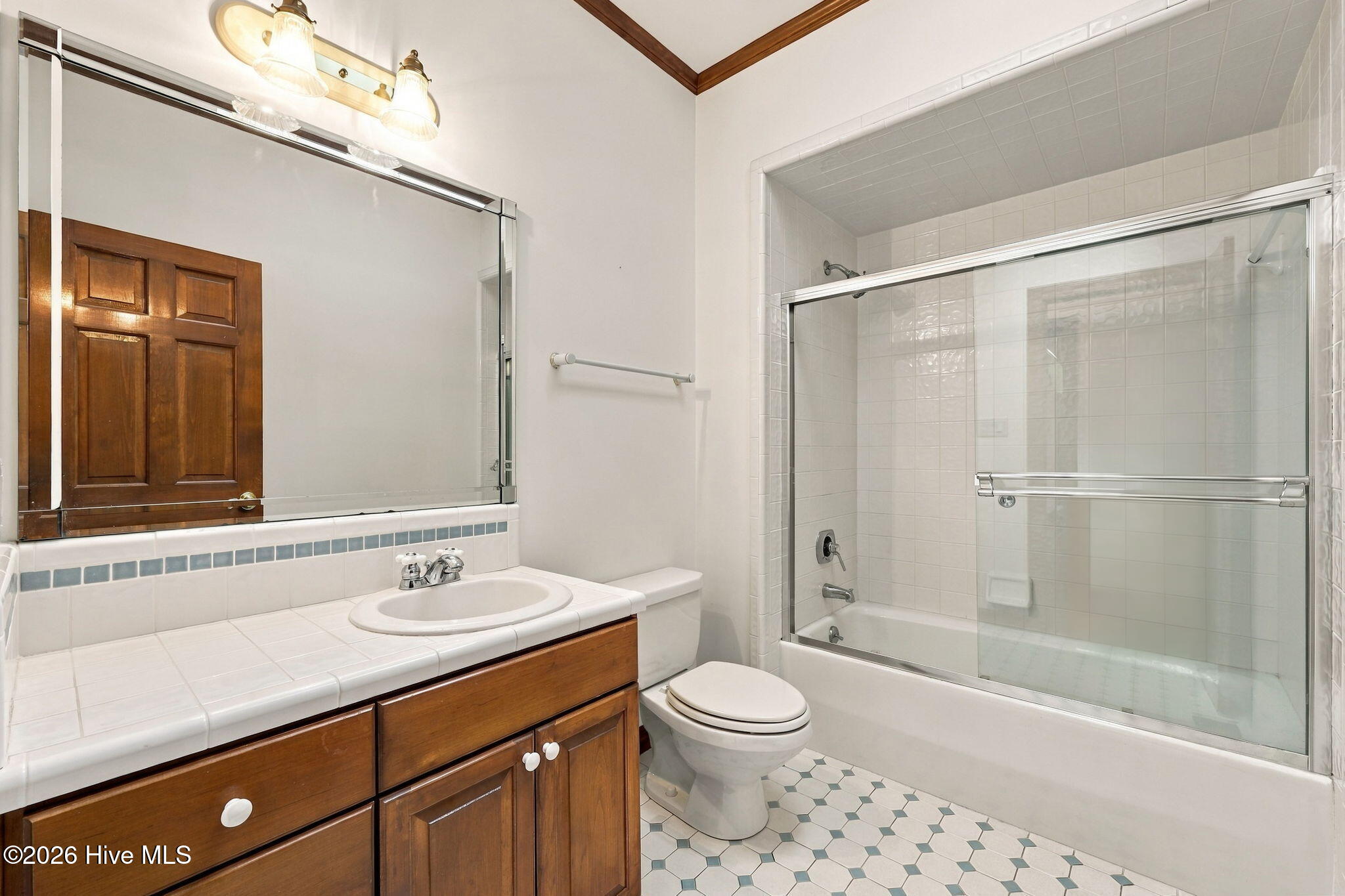 Bathroom with a wood vanity, large mirror, and tiled tub-shower with glass doors.