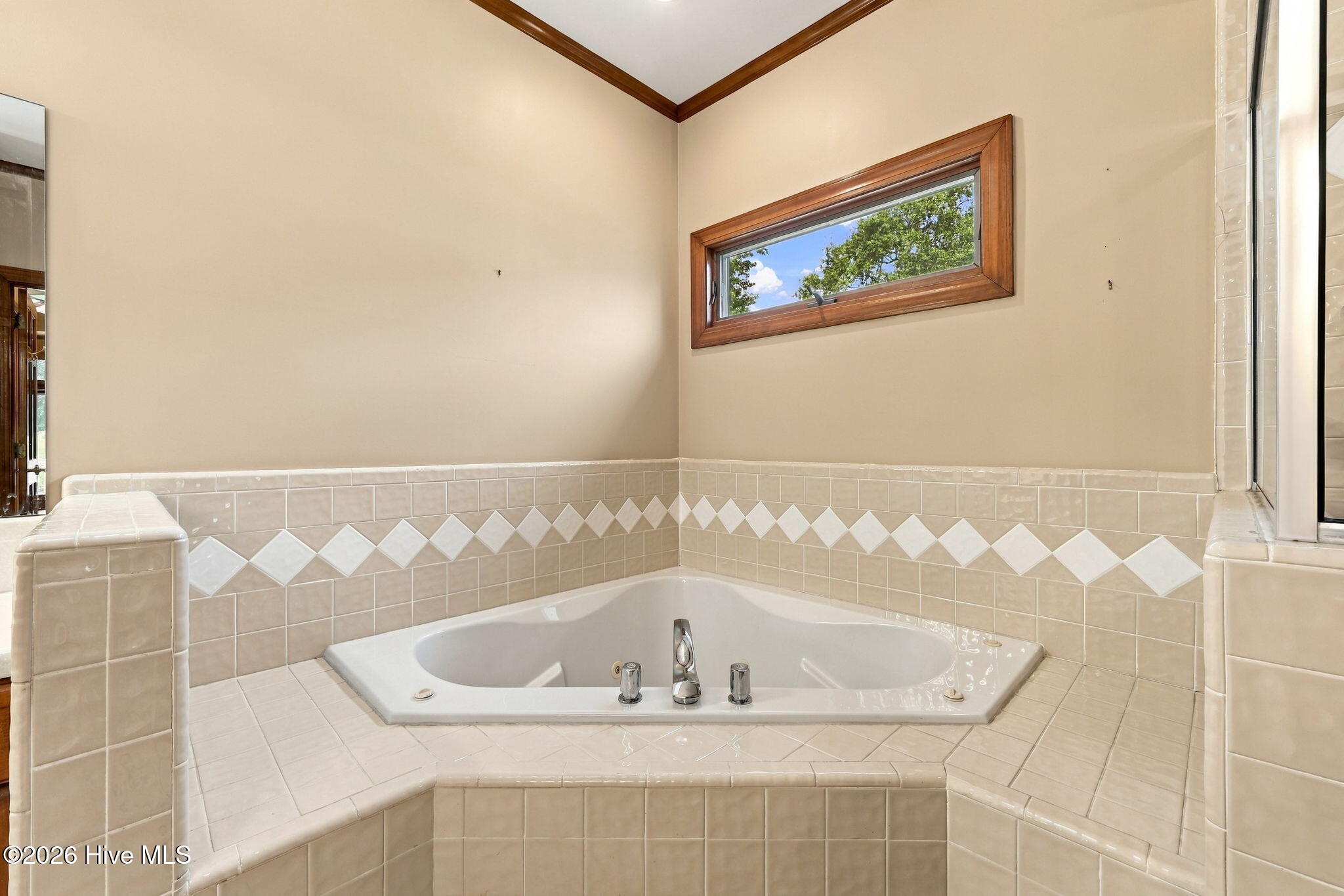 Corner soaking tub in a tiled bathroom with a diamond-pattern accent band and narrow window.