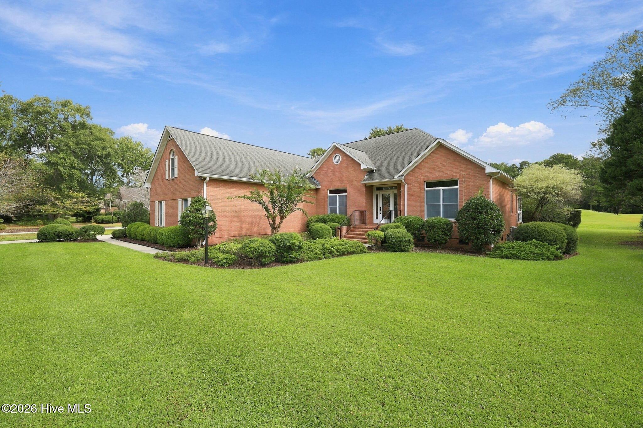 Red-brick home with a covered entry, landscaped shrubs, and a broad green lawn.