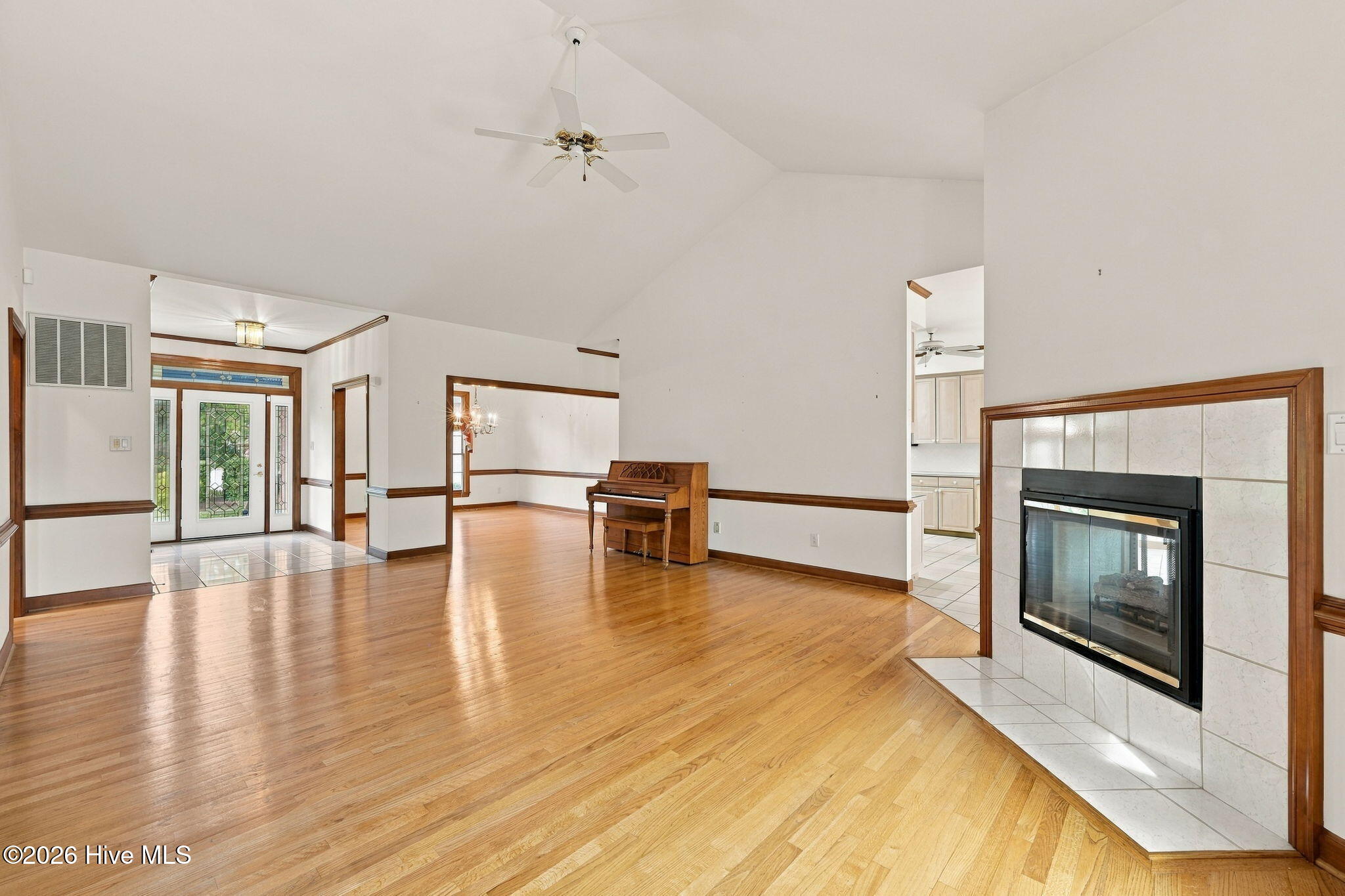 Living room with hardwood floors, a tiled fireplace, and a piano.