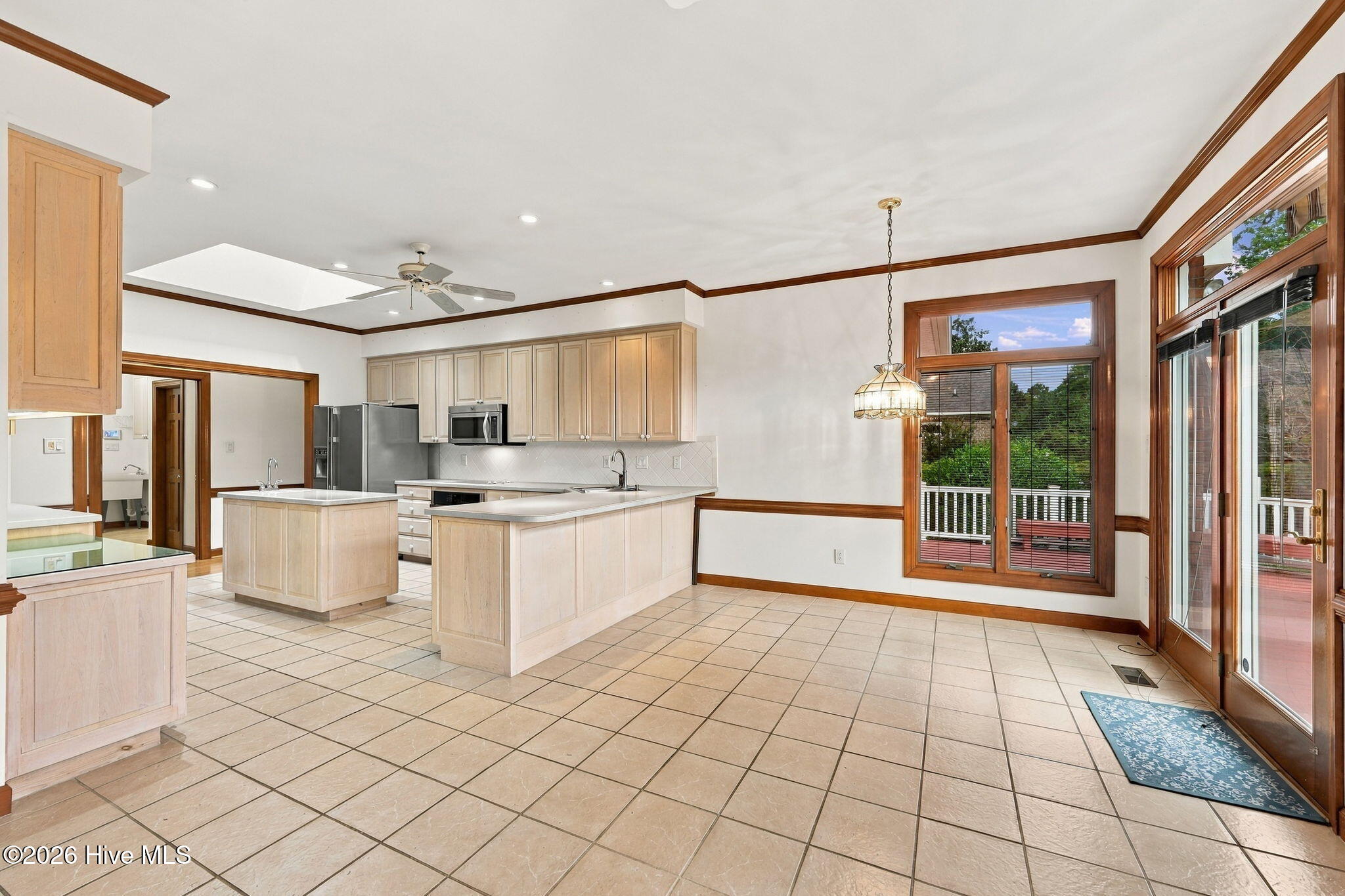 Kitchen and dining area with two islands, pale wood cabinets, tiled floors, and large windows overlooking a deck.