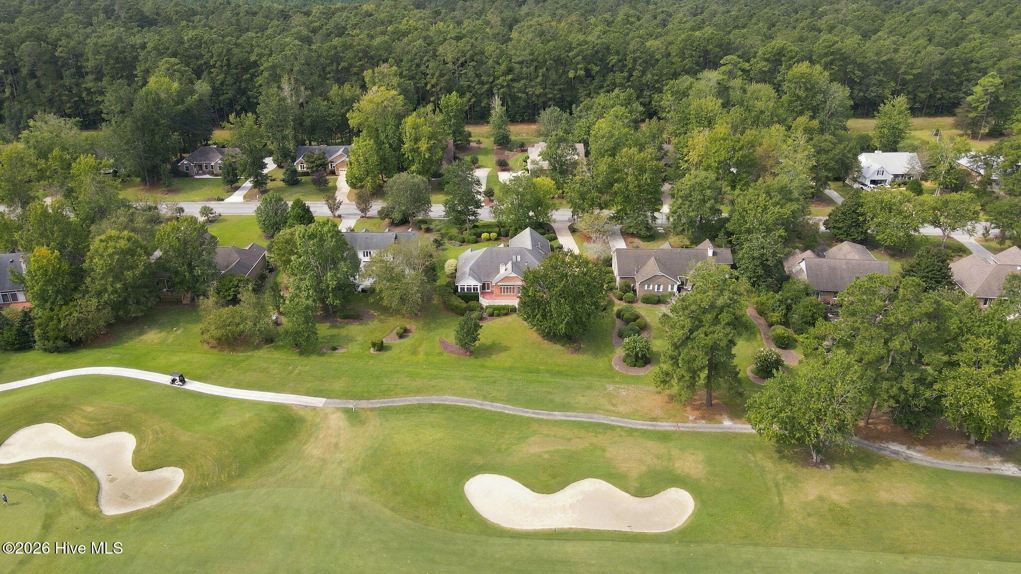 Aerial view of homes beside a golf course, with sand bunkers and woods.