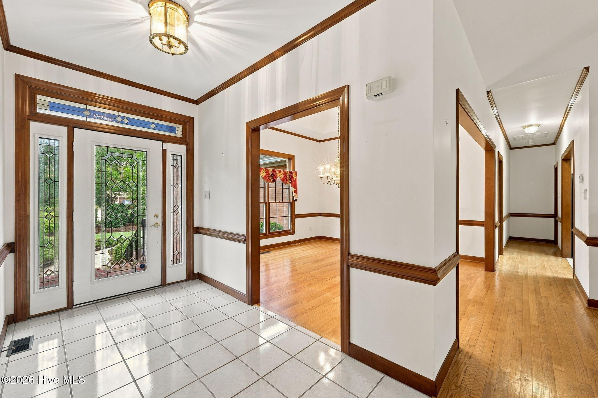 Entry foyer with decorative glass front door, tiled floor, dark wood trim, and adjoining hardwood hallway.