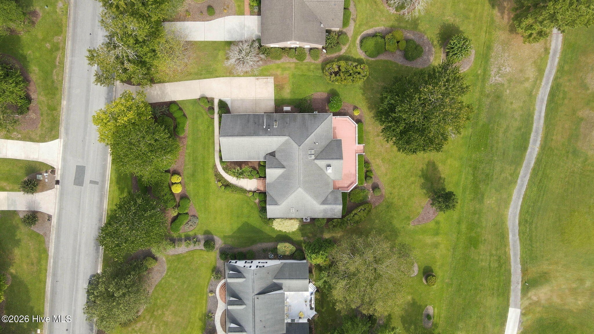 Aerial view of a house with a pink deck and landscaped lawn surrounded by mature trees.