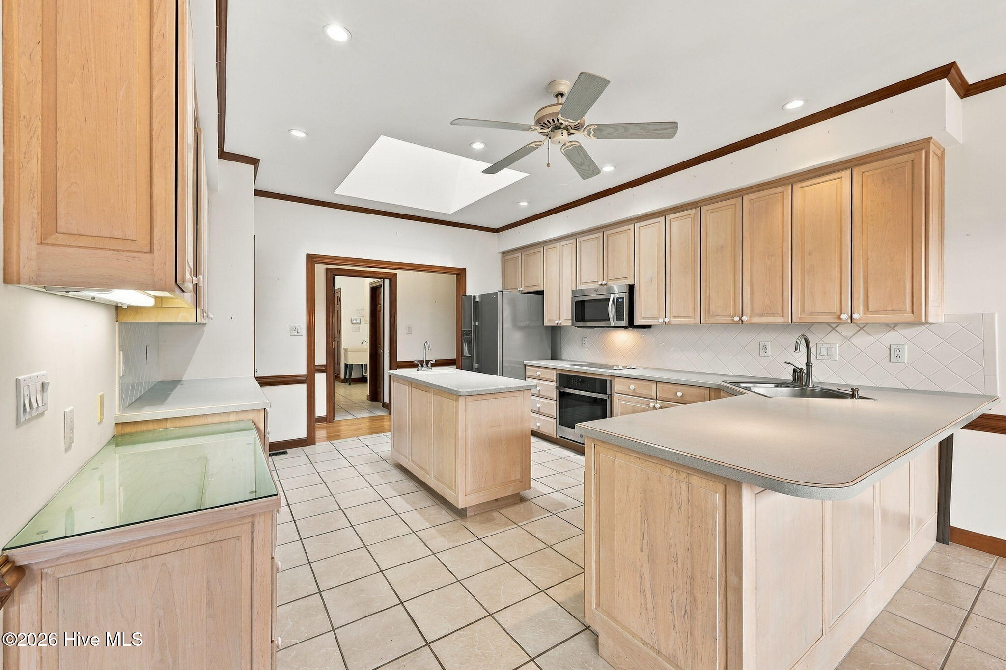 Kitchen with light wood cabinetry, two islands, stainless steel appliances, and a skylight.