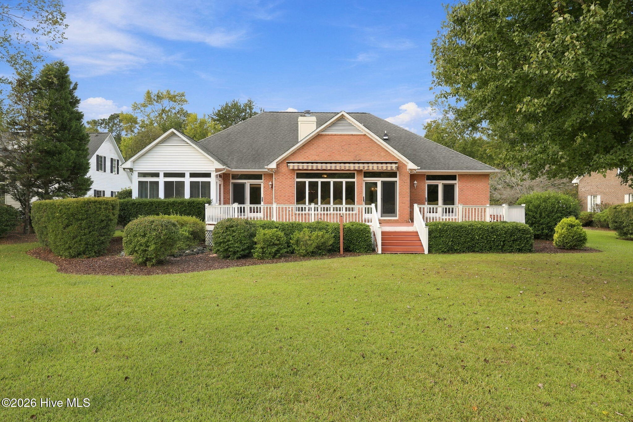 Red-brick house with a wide white-railed deck, central steps, and a spacious lawn.