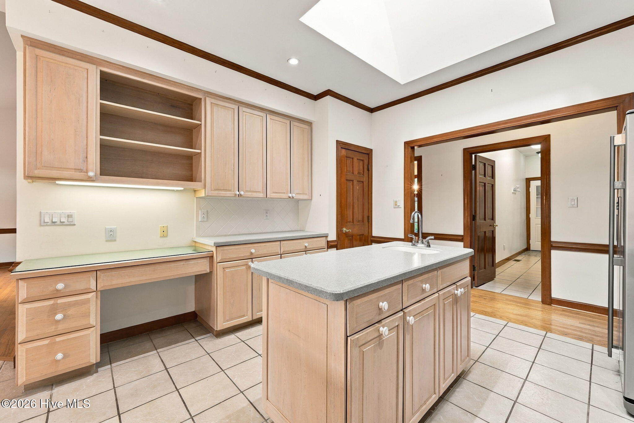 Kitchen with a large sink island, light wood cabinetry, tiled floors, and a skylight.