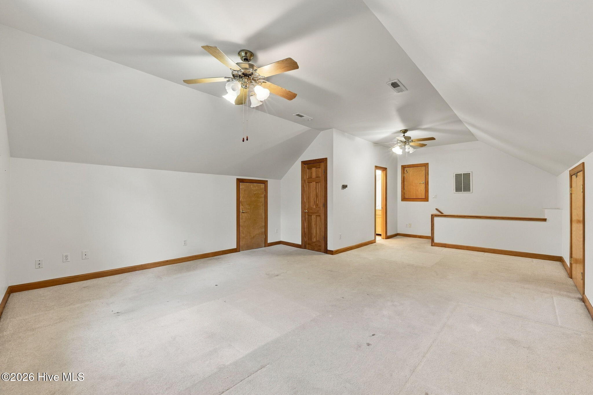 Vacant carpeted room with a high sloped ceiling, two ceiling fans, and wood-trimmed doors.