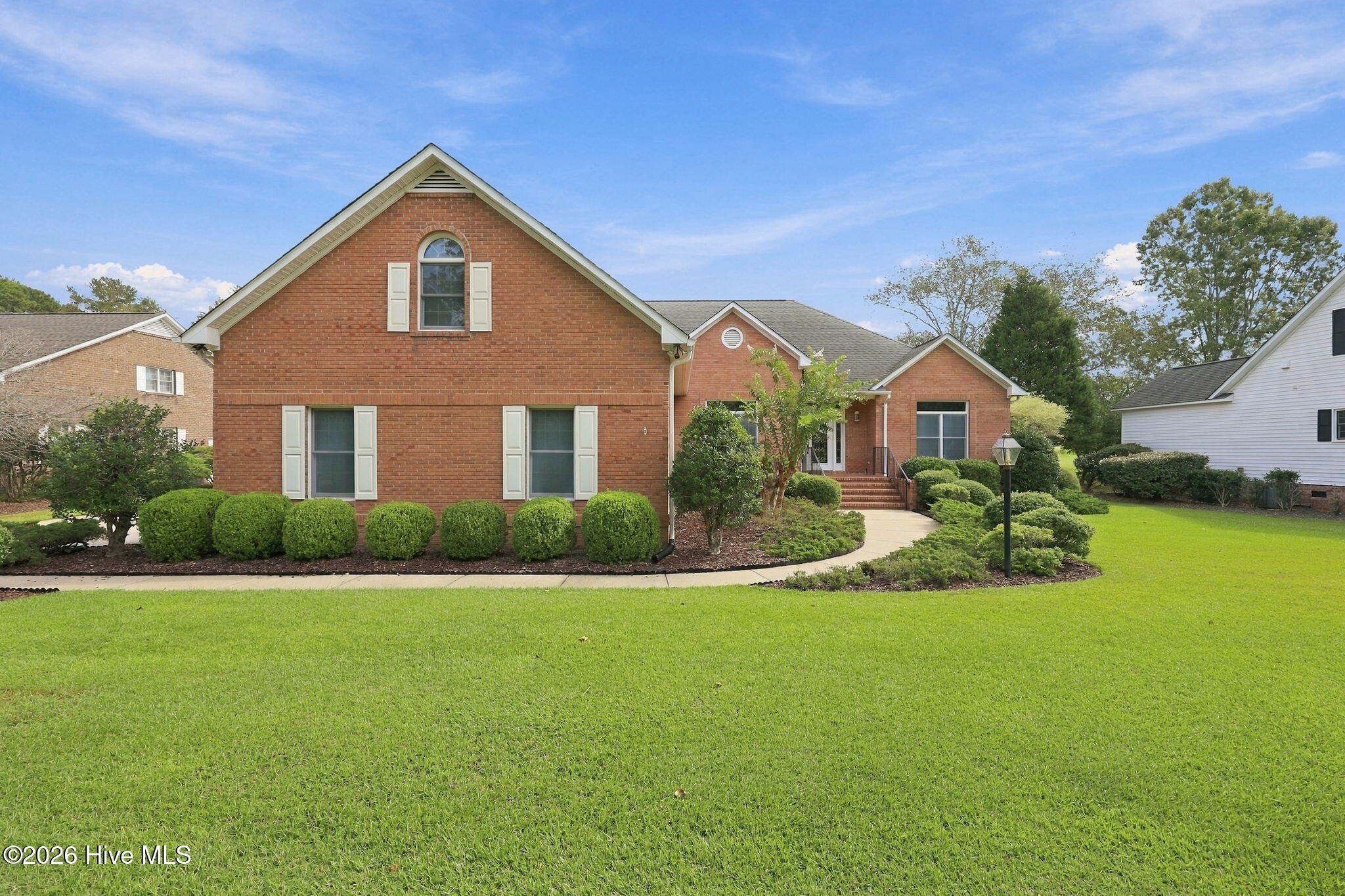 Red-brick home with a prominent gable, landscaped shrubs, curved walkway, and broad front lawn.