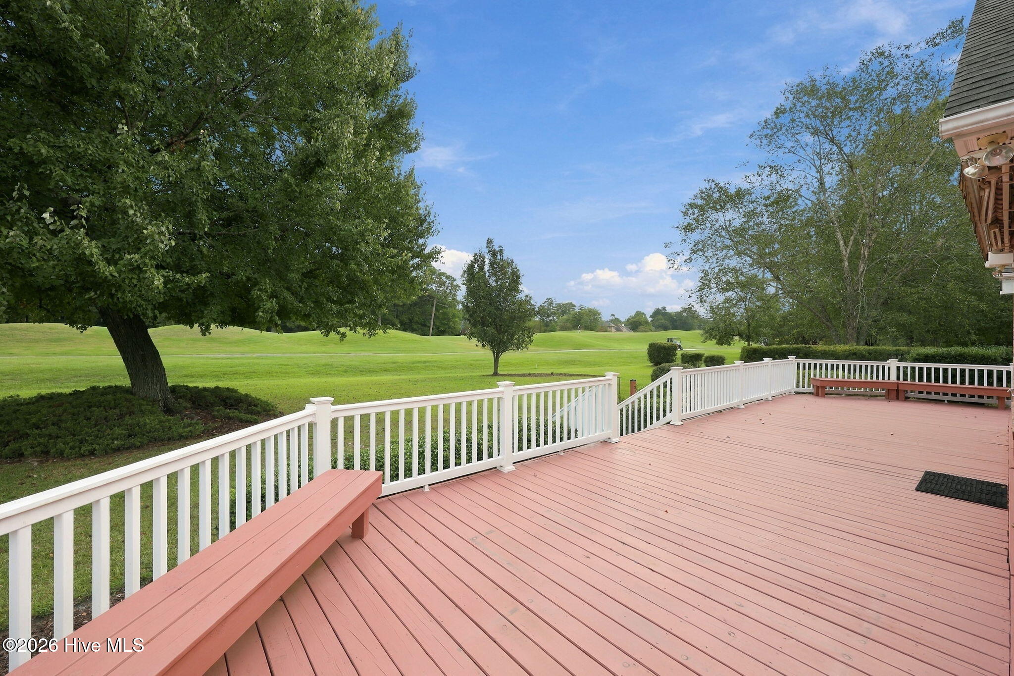 Spacious deck overlooking a golf course, with white railings and built-in benches.