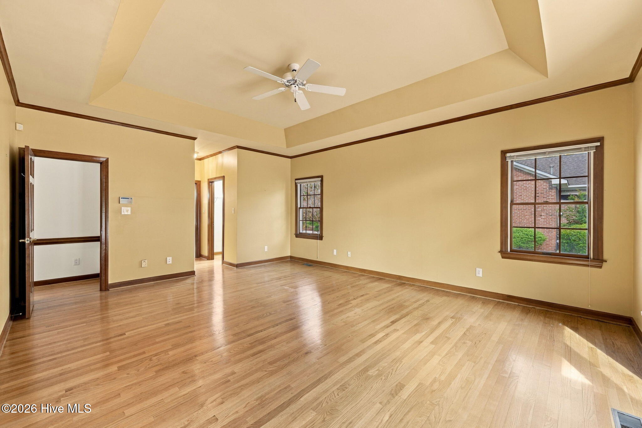 Empty living room with hardwood floors, a tray ceiling, and dark wood-trimmed windows.
