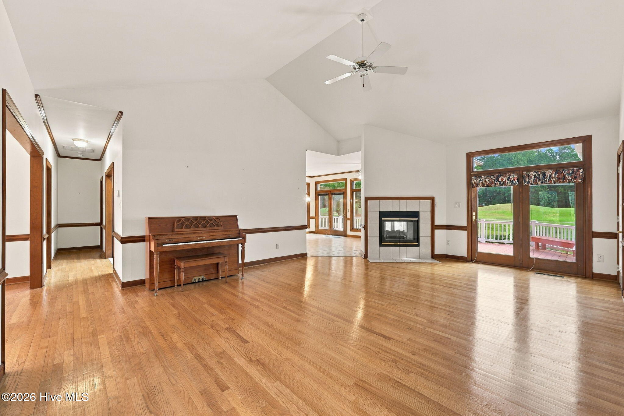 Living room with hardwood floors, an upright piano, tiled fireplace, and glass doors to a deck.