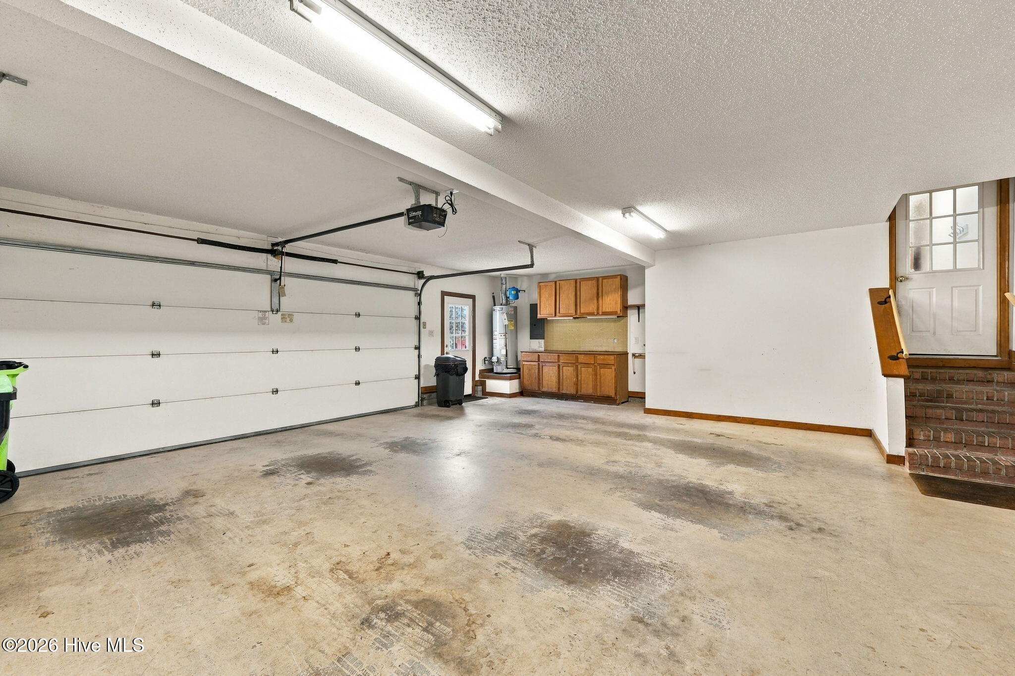 Garage with a stained concrete floor, wooden storage cabinets, and brick steps to an entry door.