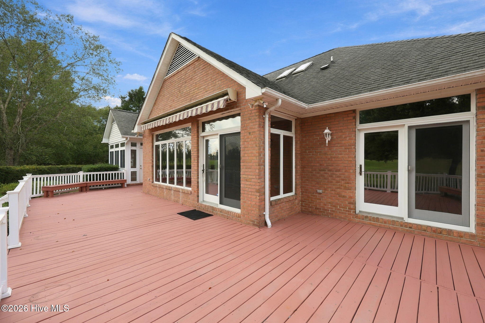 Spacious pink deck beside a red-brick house, with white railings and multiple glass doors.